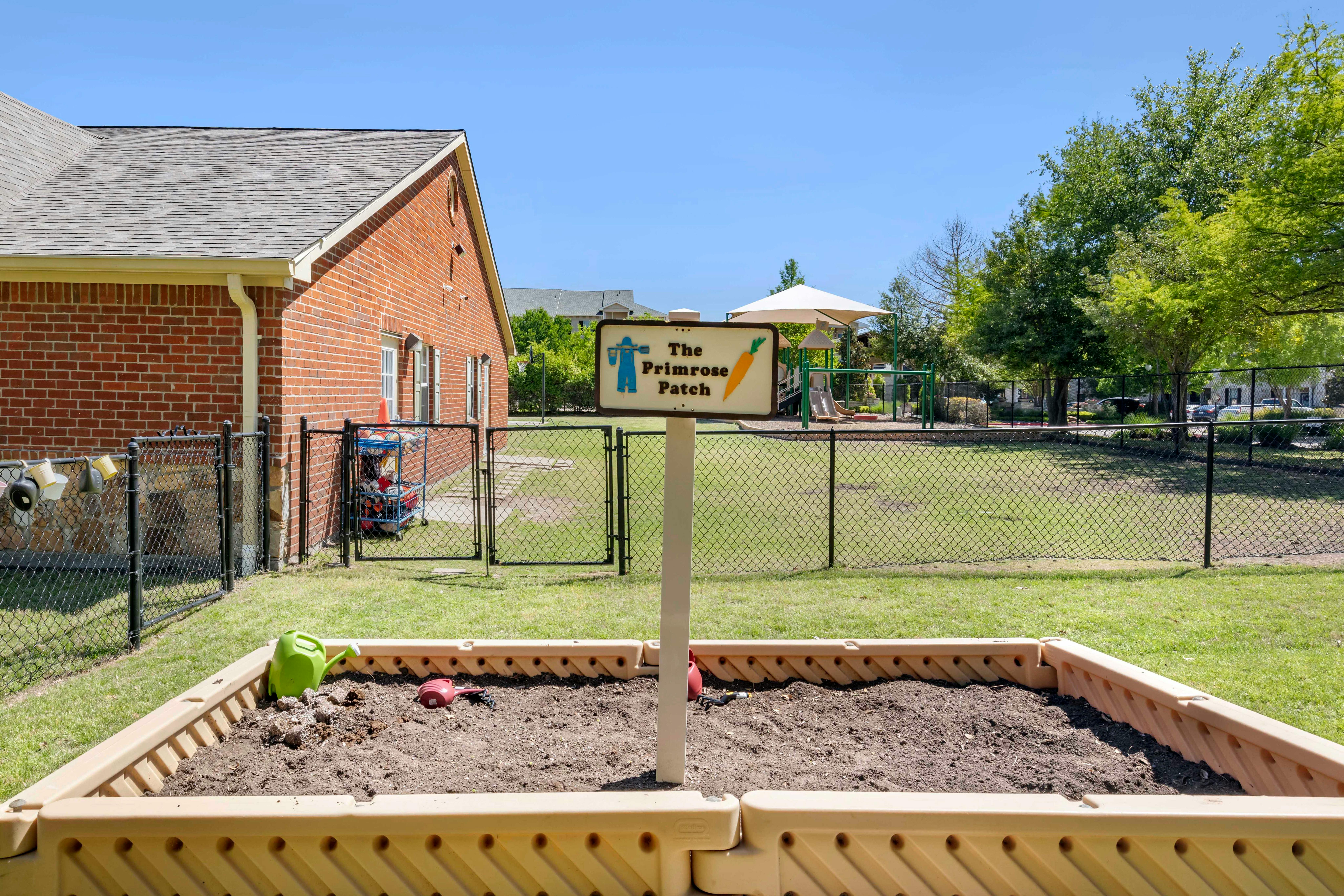 Raised garden bed with a sign for "The Primrose Patch" and a playground in the background