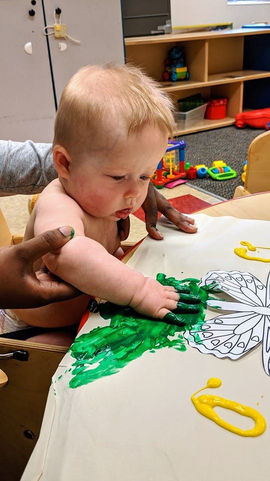 Child finger painting with green paint on paper