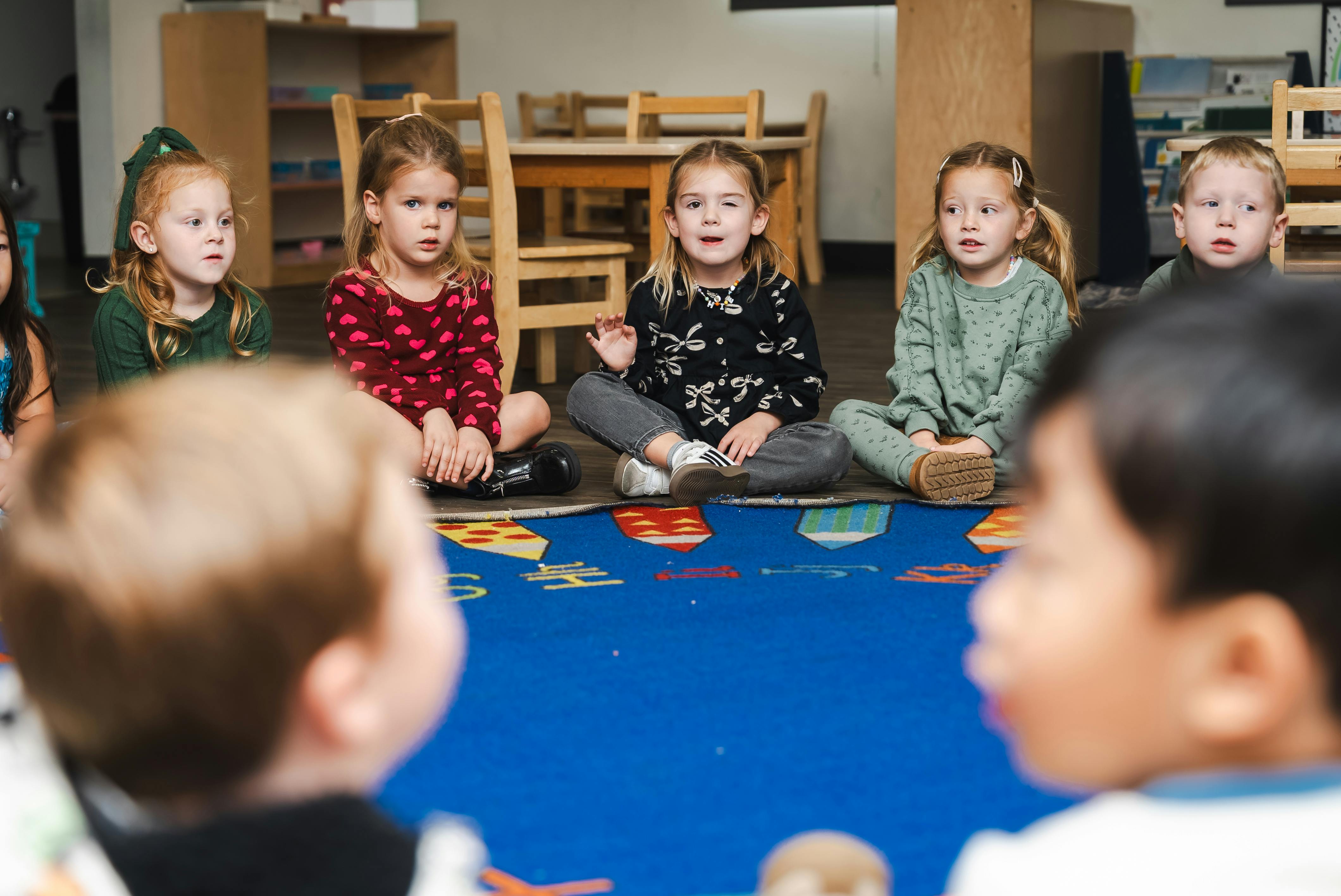 Children sitting on a blue rug in a classroom