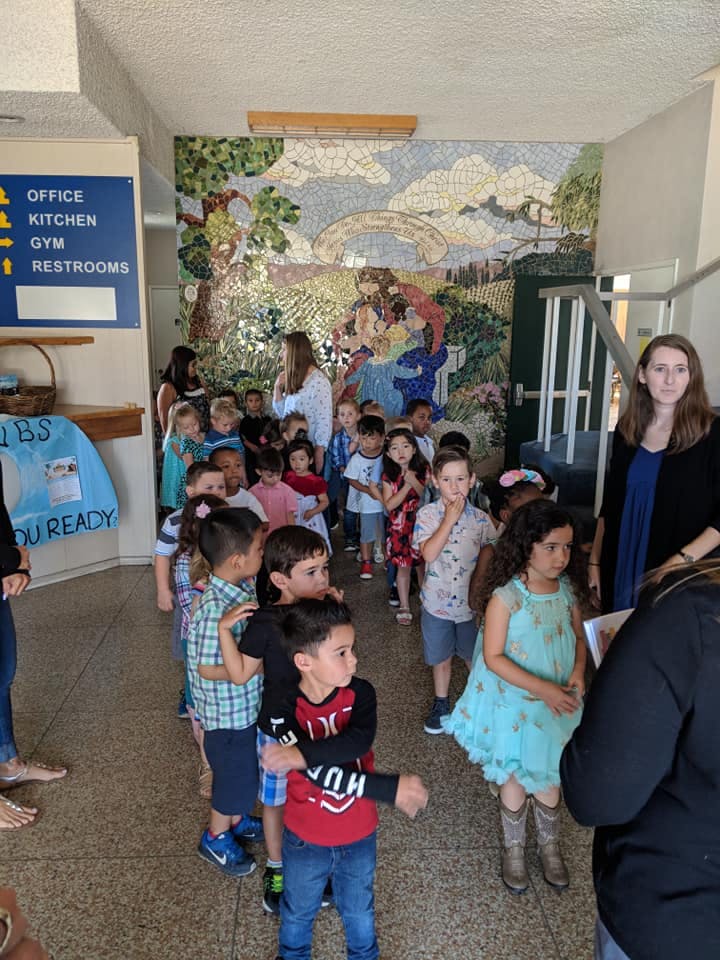 Adults supervising a line of children in a hallway