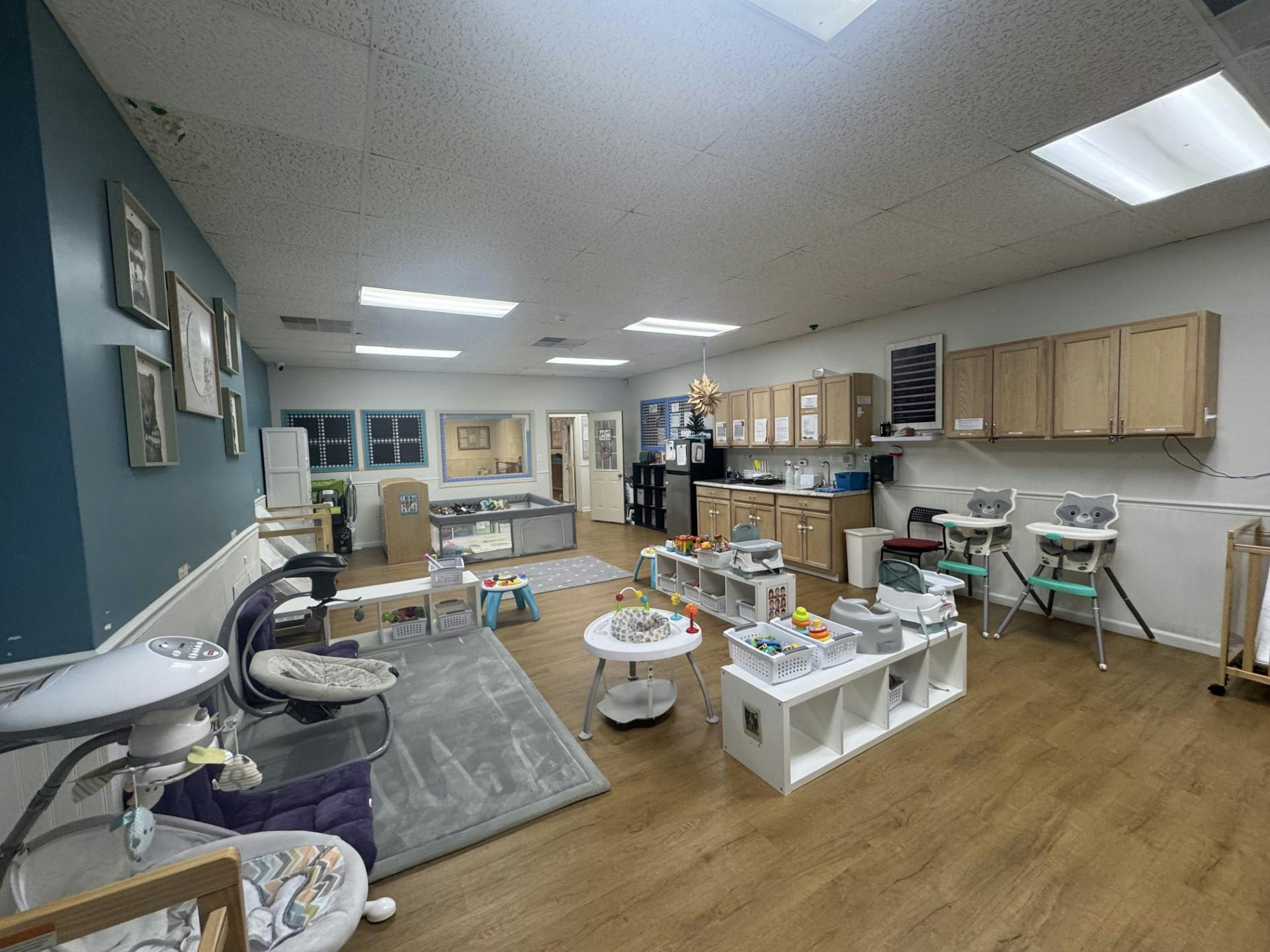 A classroom for infants and toddlers with baby swings, high chairs, and play mats