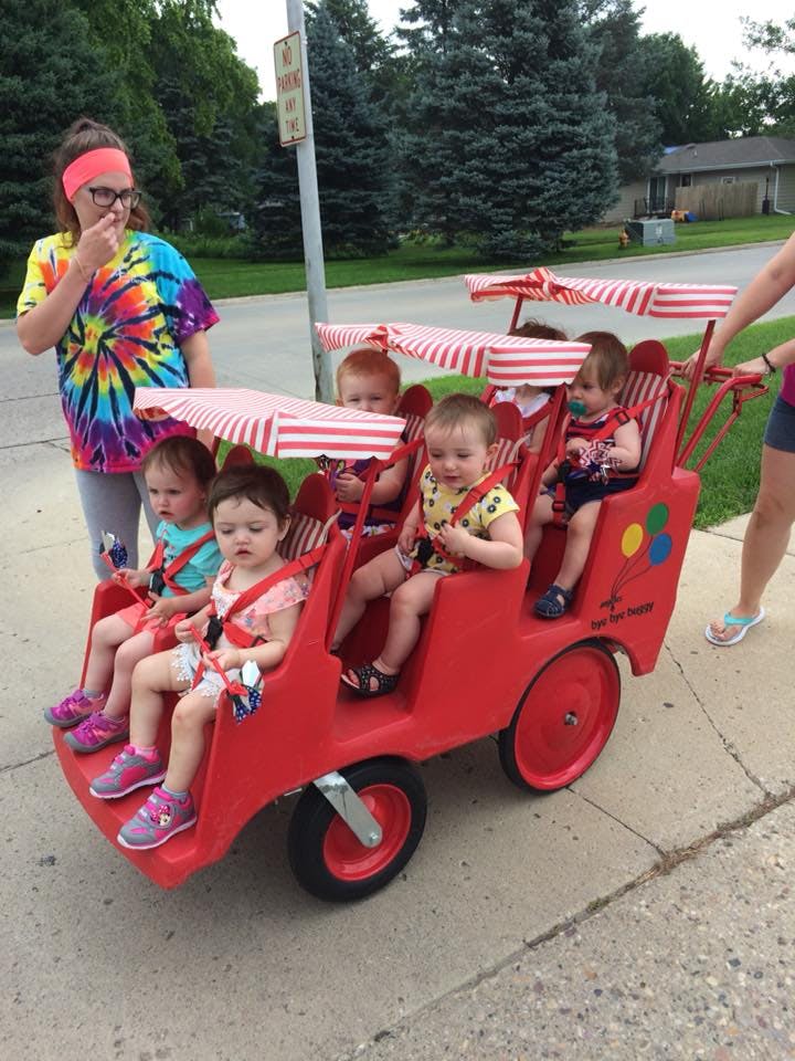 Person standing next to a multi-child stroller with several children inside