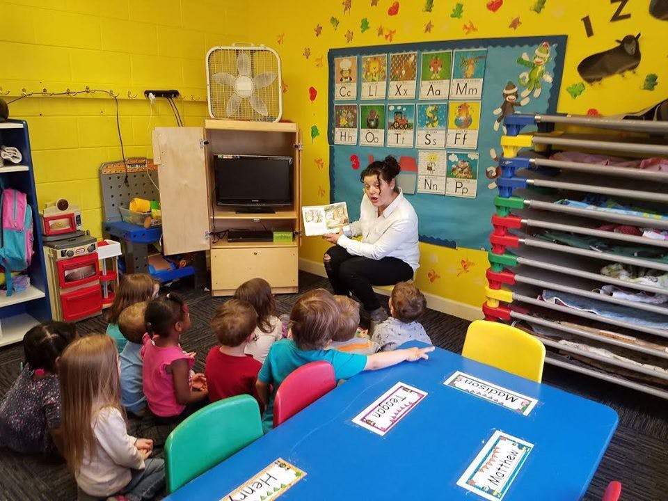 Person reading a book to a group of children in a classroom