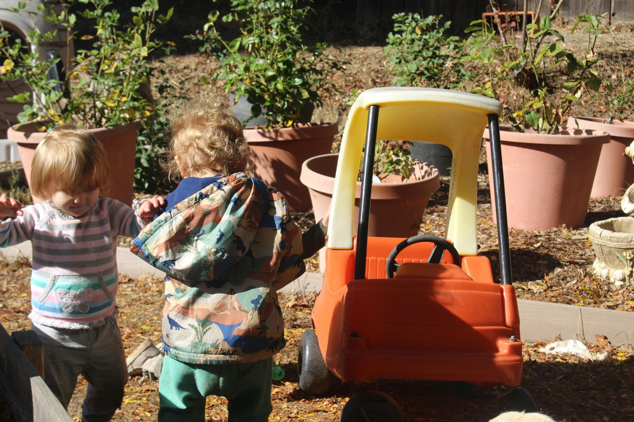 Two children standing near a toy car outdoors