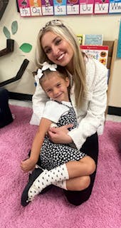 Adult and child posing together in a classroom