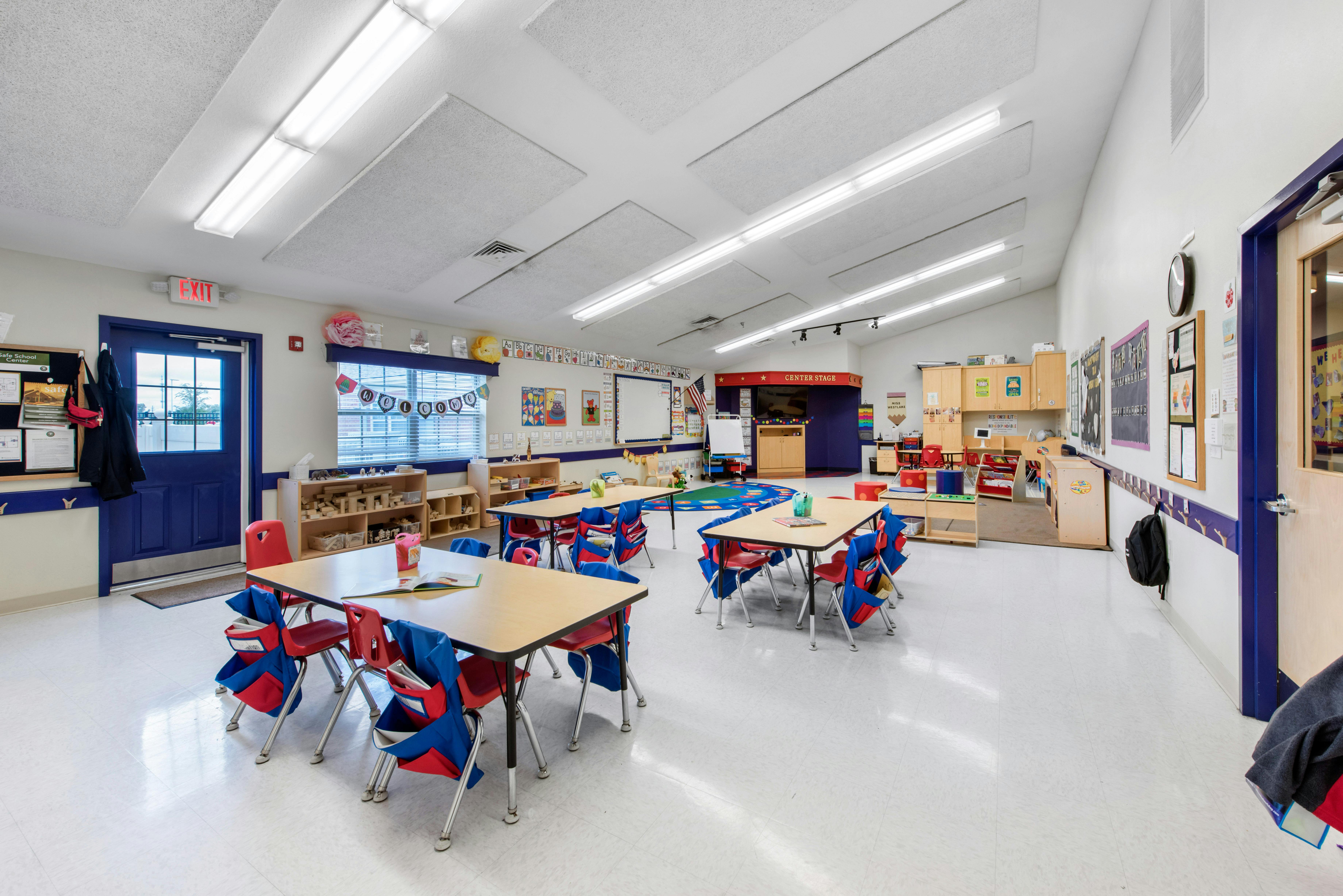 Classroom with small tables and chairs, an exit sign, and learning displays