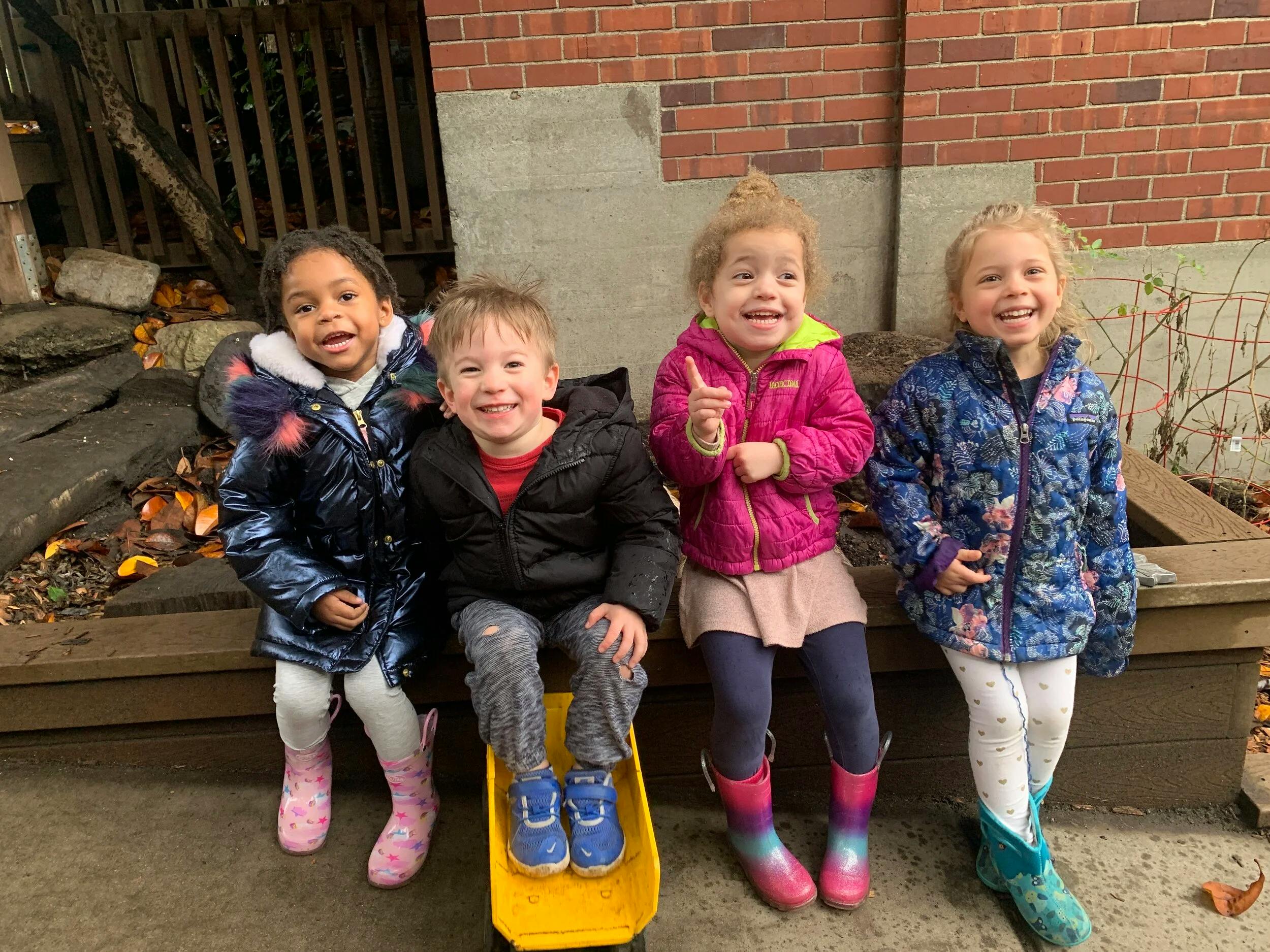 Four children in winter coats sitting on a wooden bench