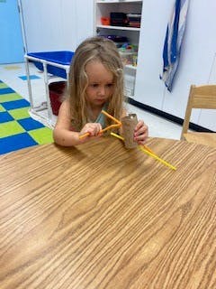 Child playing with craft sticks and a cardboard tube at a table