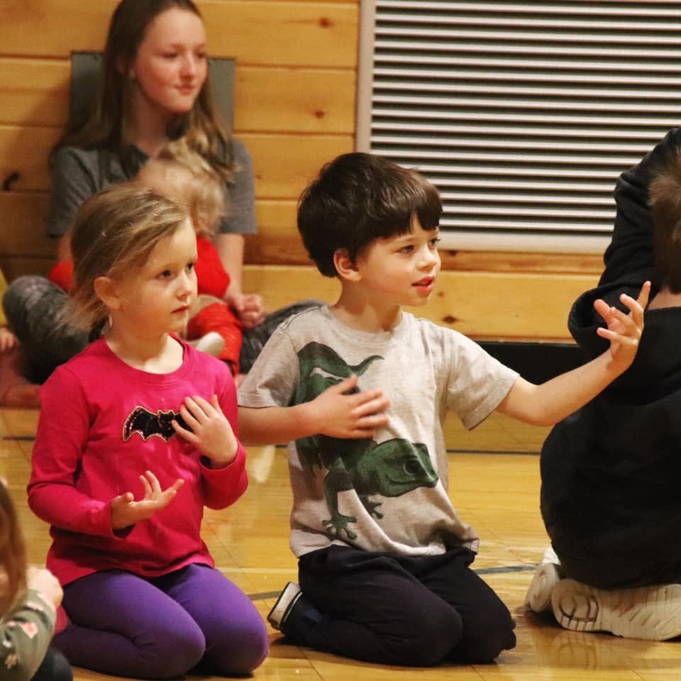 Two children kneeling and gesturing with their hands