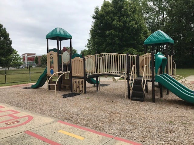 A tan and green playground structure with multiple slides on wood chips