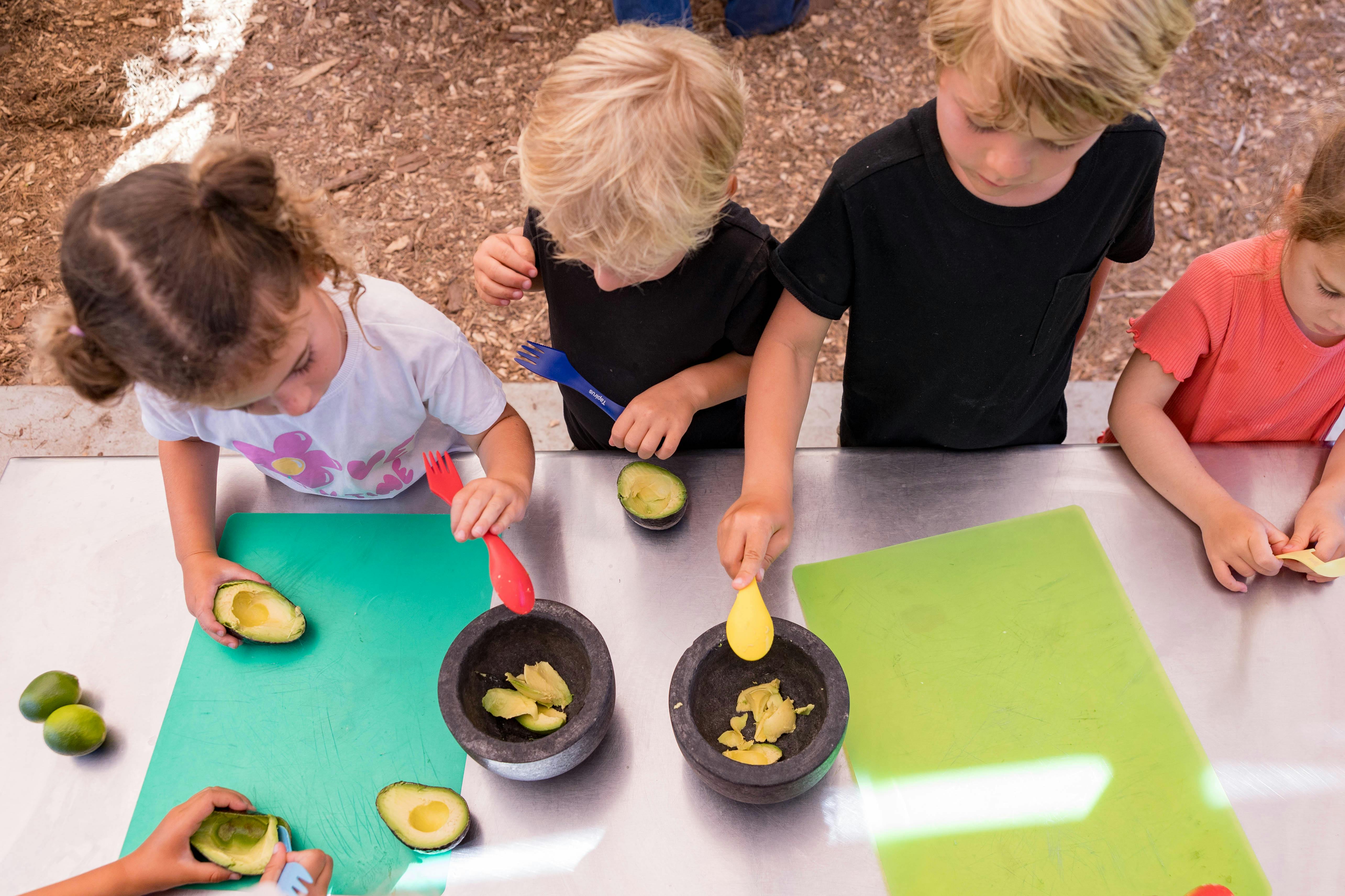 Four children preparing avocados at a metal table