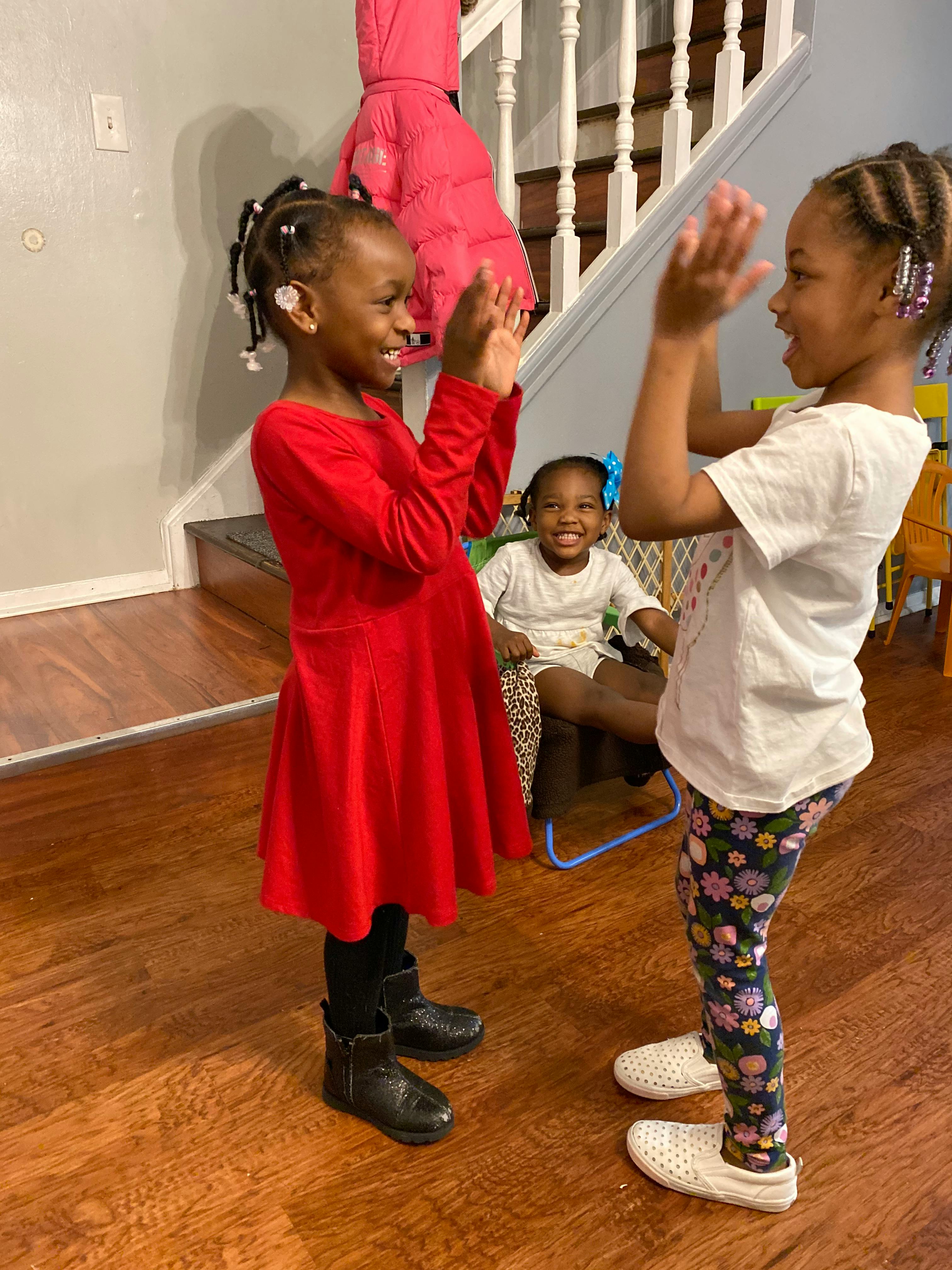Two children playing patty-cake, another child seated in the background