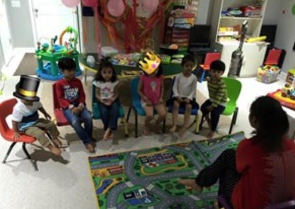 Children sitting in a circle on chairs and a person on the floor