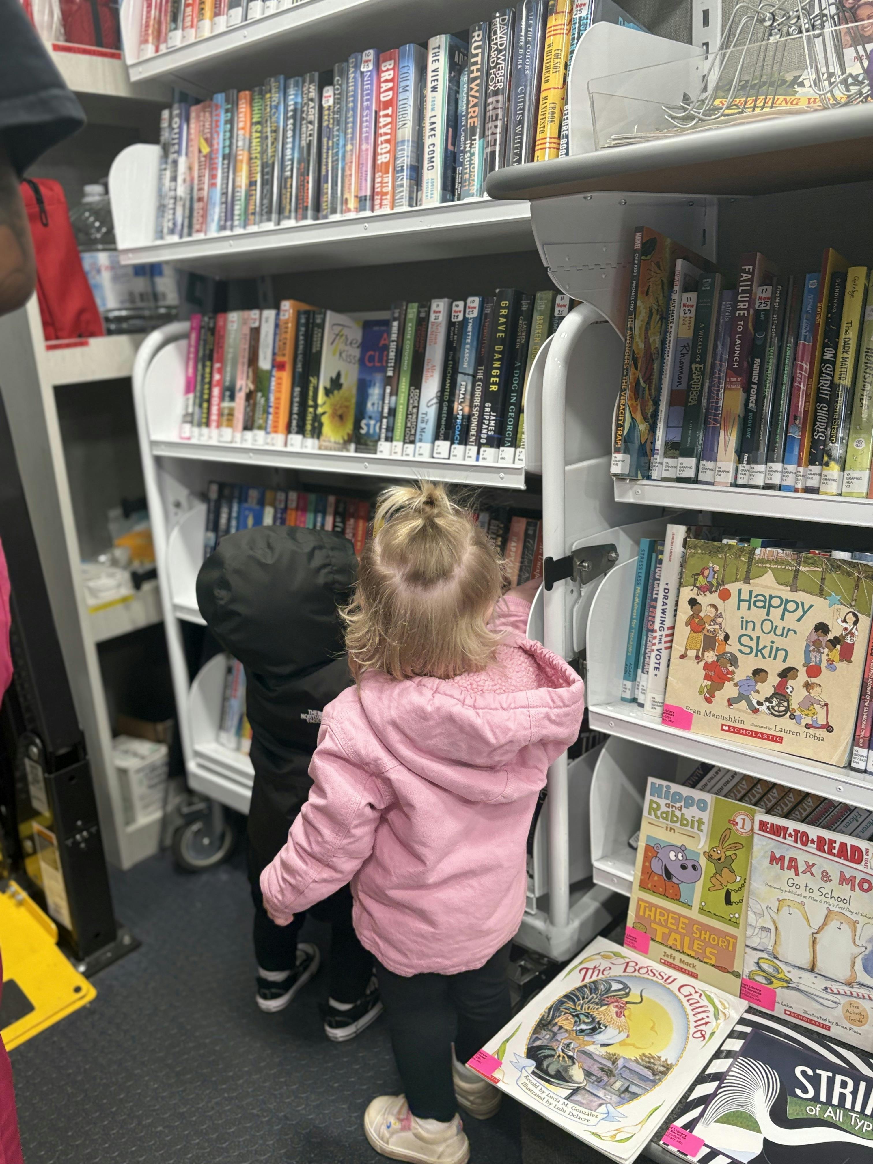Two children looking at books on shelves in a library