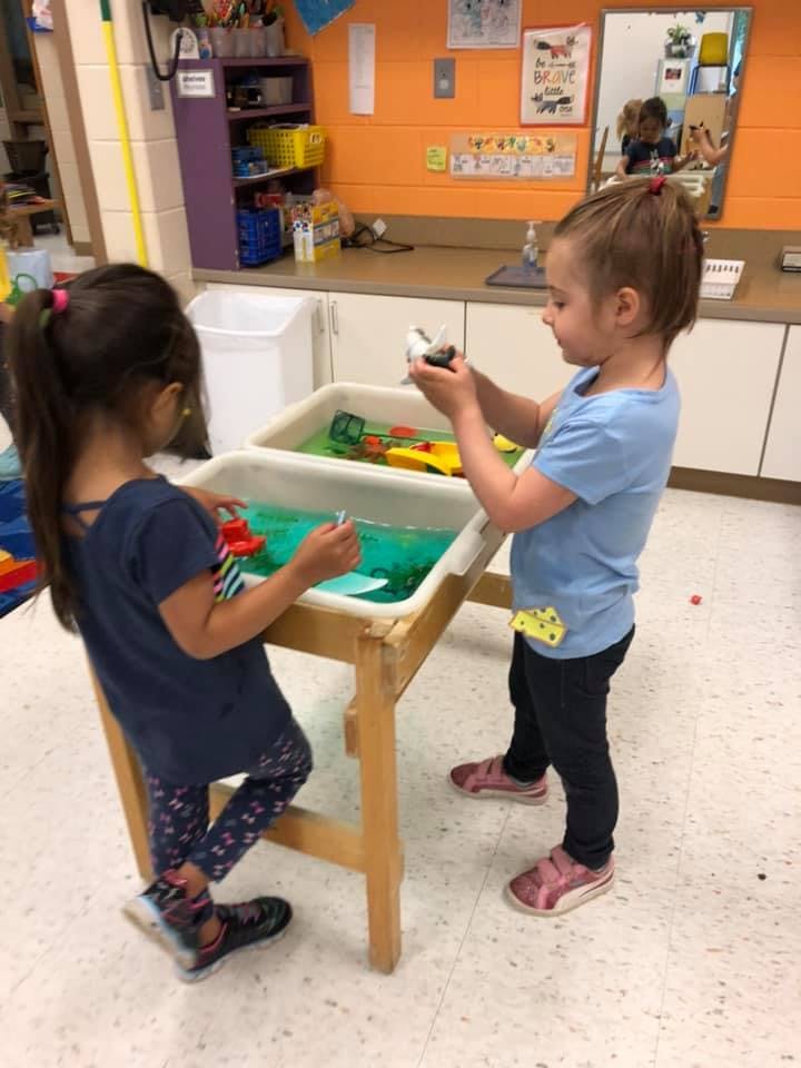 Two children playing at a water table in a classroom