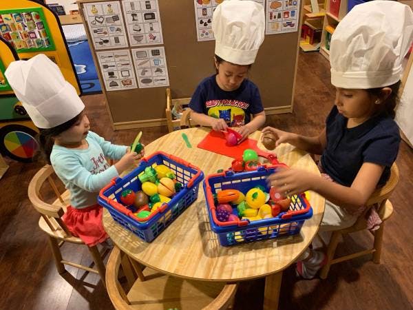 Three children wearing chef hats playing with toy food at a table