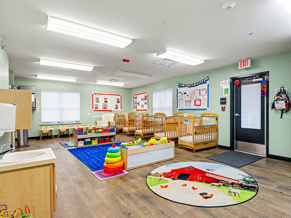 A brightly lit nursery classroom with multiple cribs and a play area