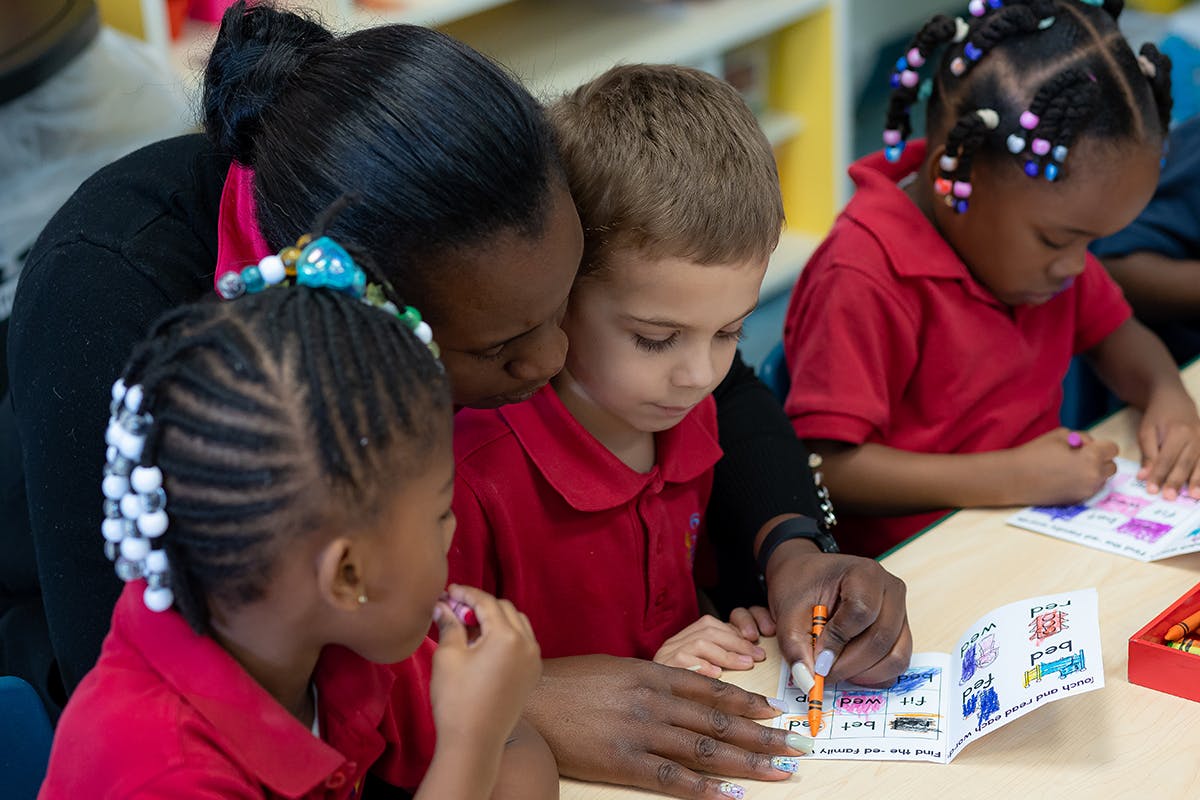 Adult helping three children with an activity book at a table