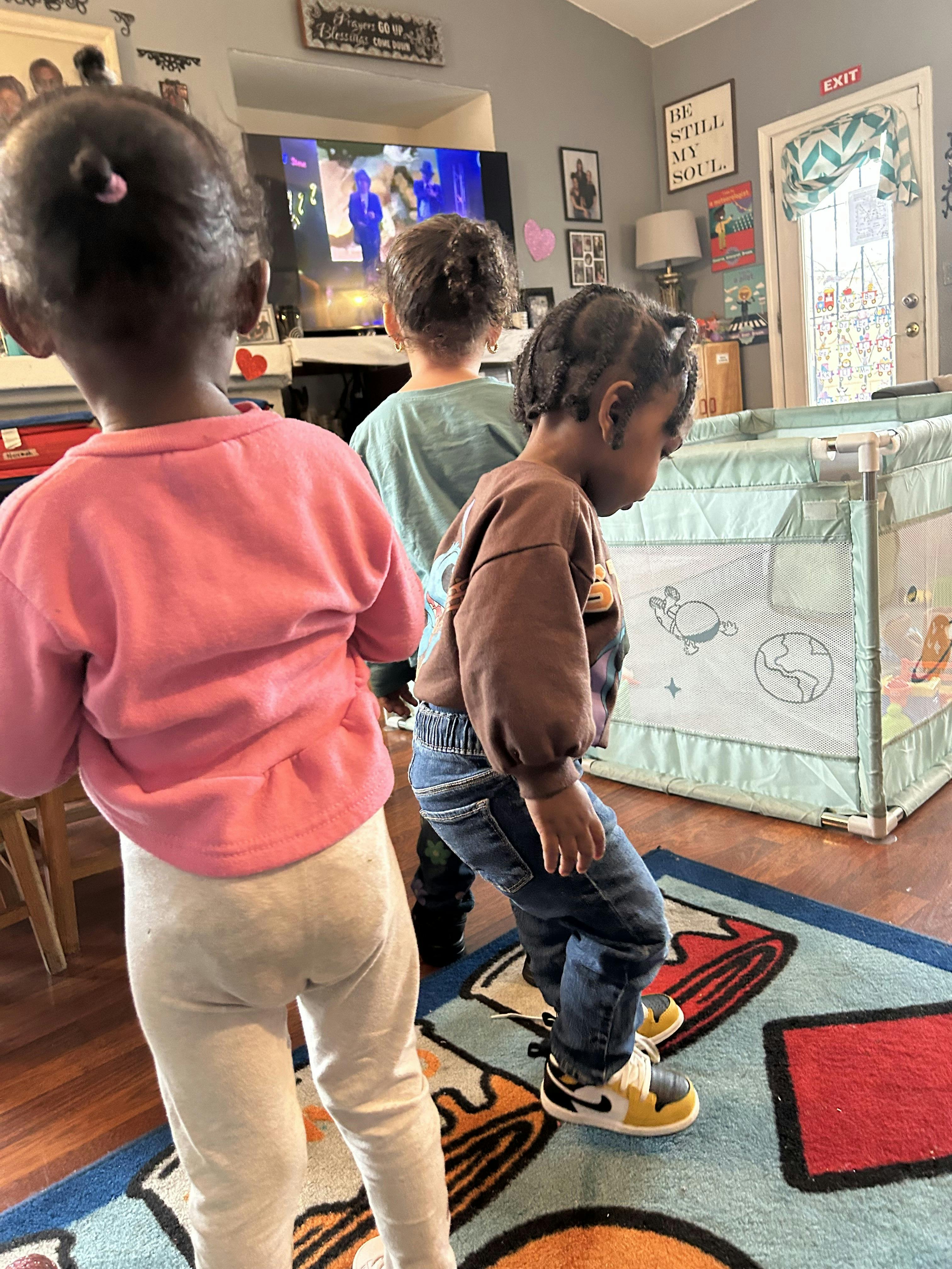 Three children in a living room, two looking at a TV