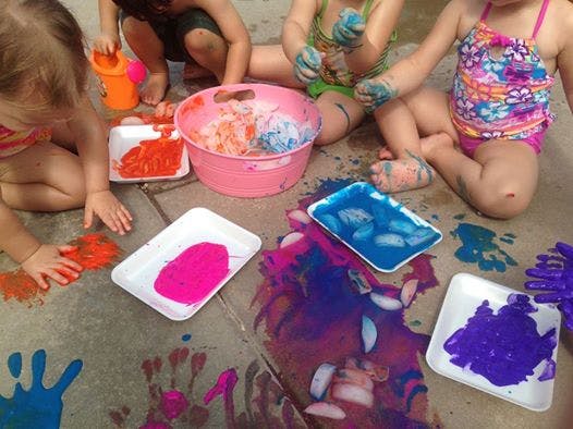 Children finger painting with colorful paint and ice on the ground