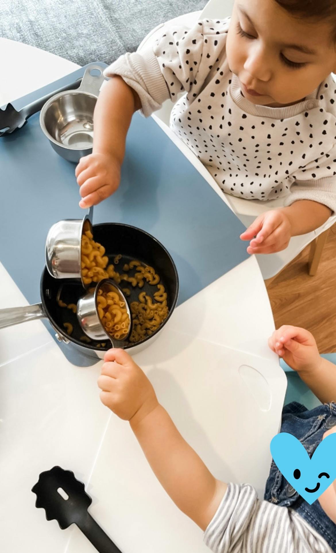 Child playing with pasta and measuring cups in a pot