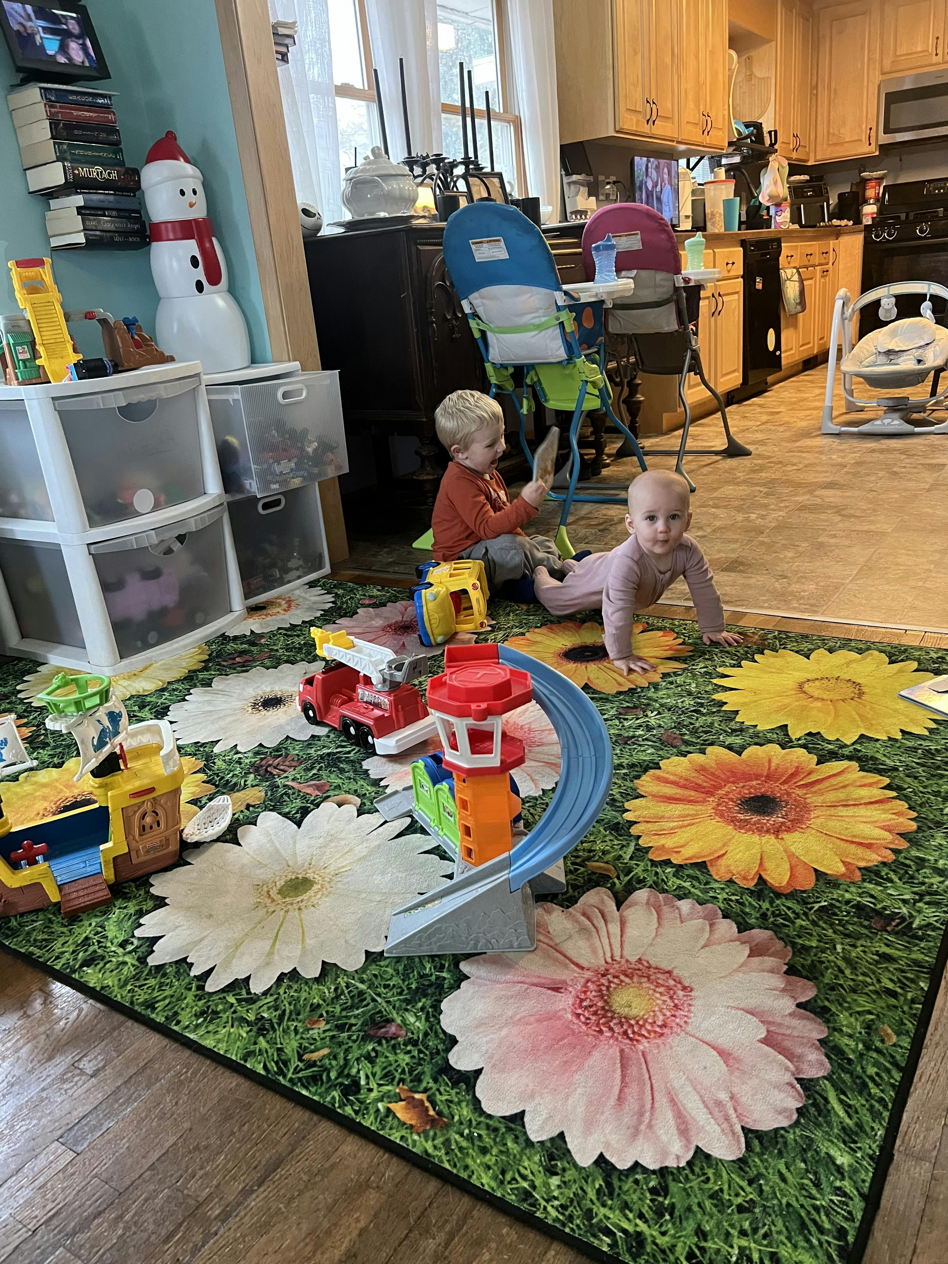 Child playing with toys on a floral rug, baby crawling nearby