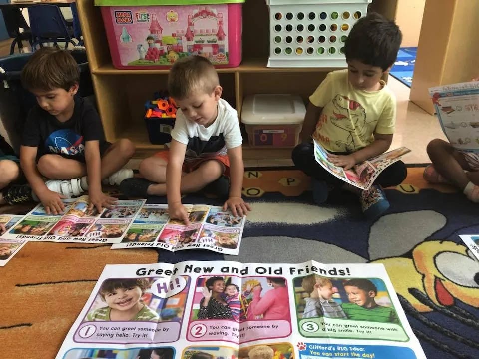 Three children sitting on a rug looking at books