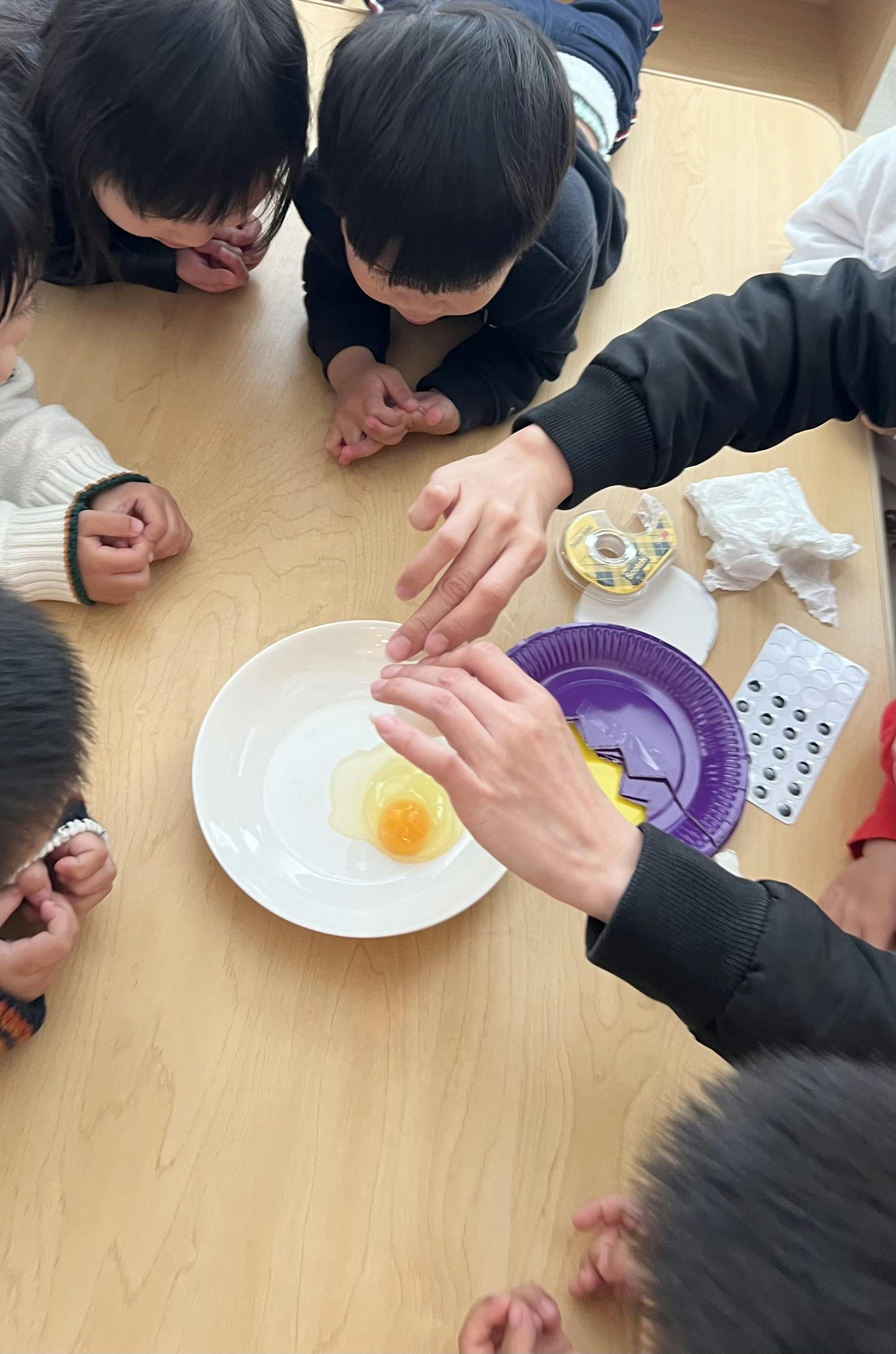 A person cracking an egg onto a white plate while children watch