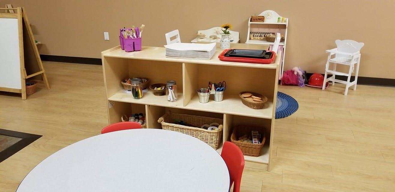 Classroom with a wooden shelf unit, white table, and red chairs