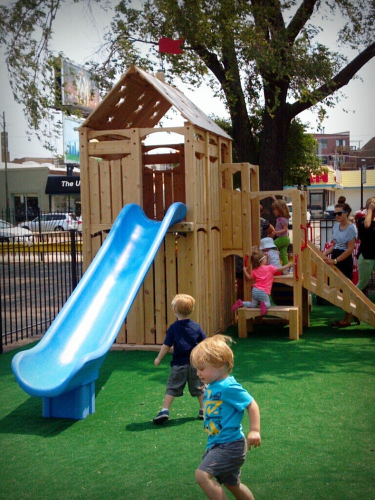Children playing on a wooden playground structure with a blue slide