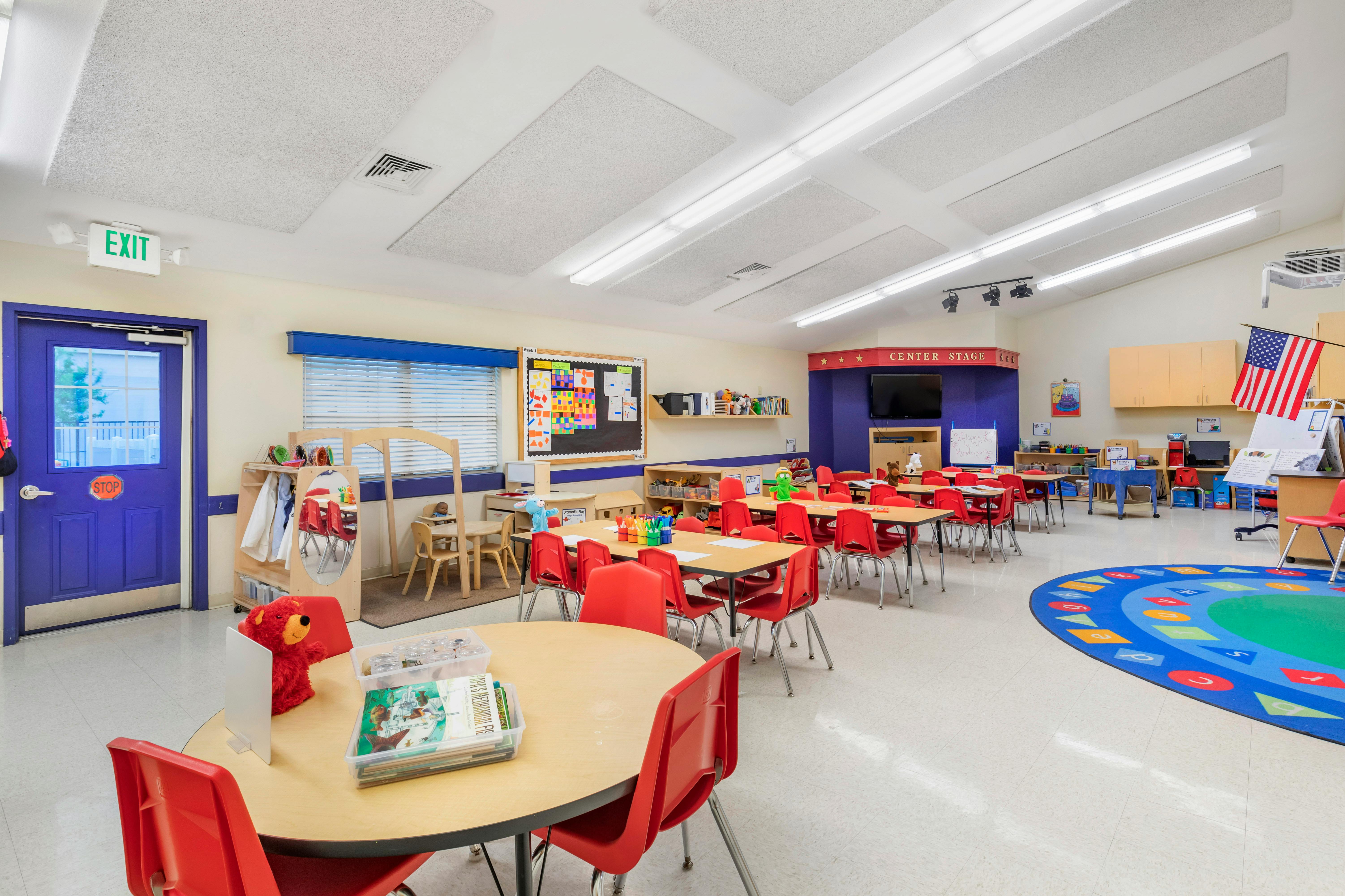 An empty elementary school classroom with small tables and red chairs