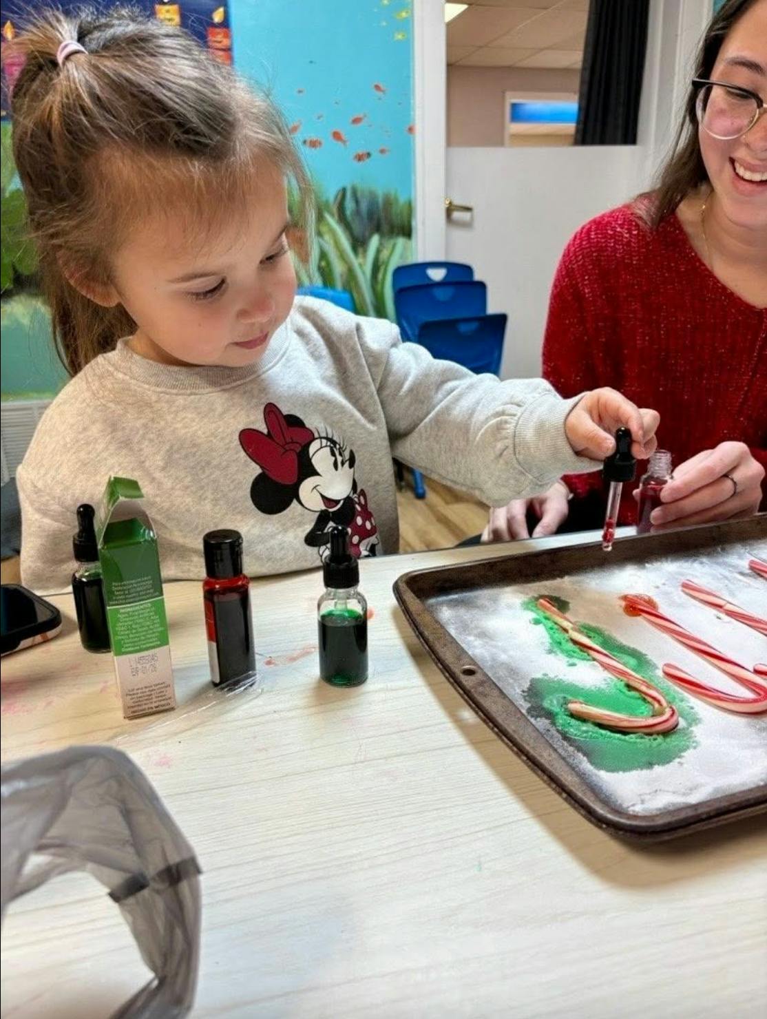 Child using a dropper to add food coloring to candy canes on a tray