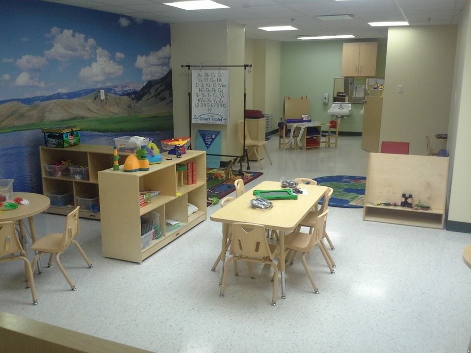 Empty classroom with small tables and chairs, shelves with toys and toys