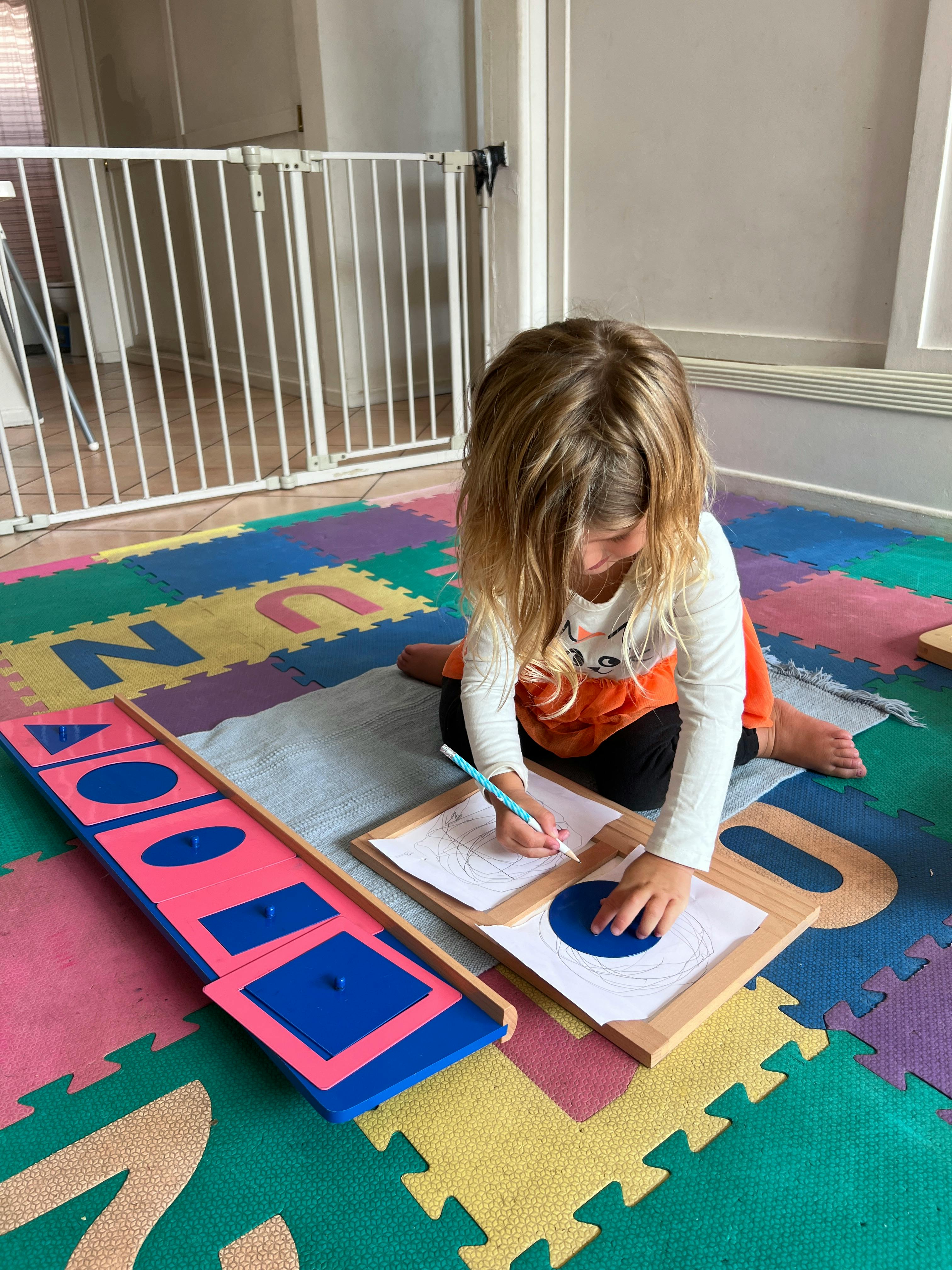Child drawing on paper with a pencil, using a shape stencil
