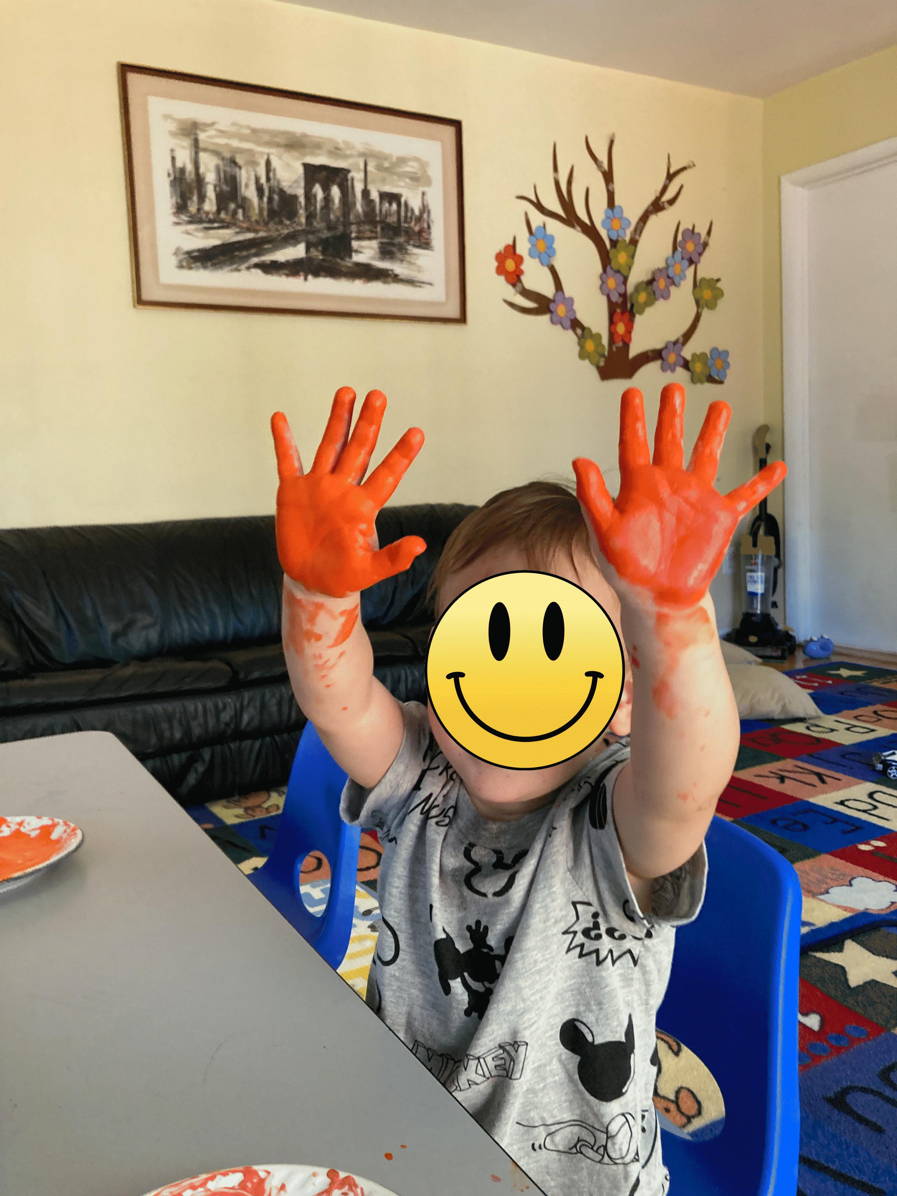 Child sitting at a table with orange paint on their hands