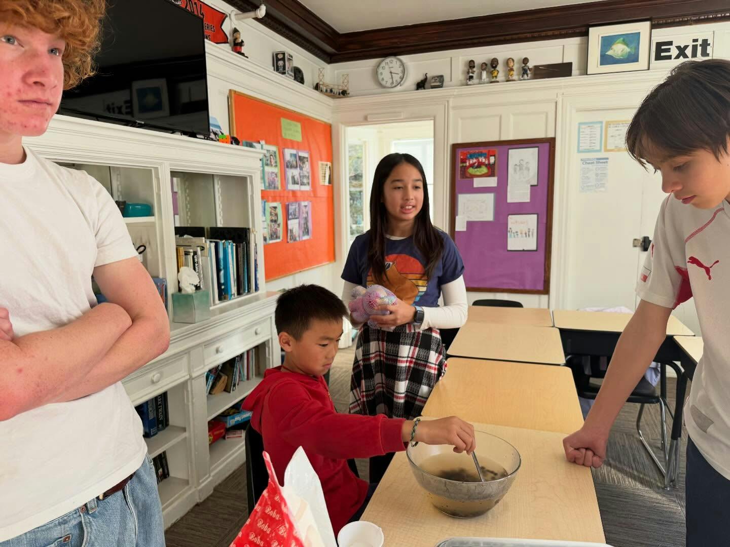 Three teens and a child looking at a bowl on a desk with a spoon in it