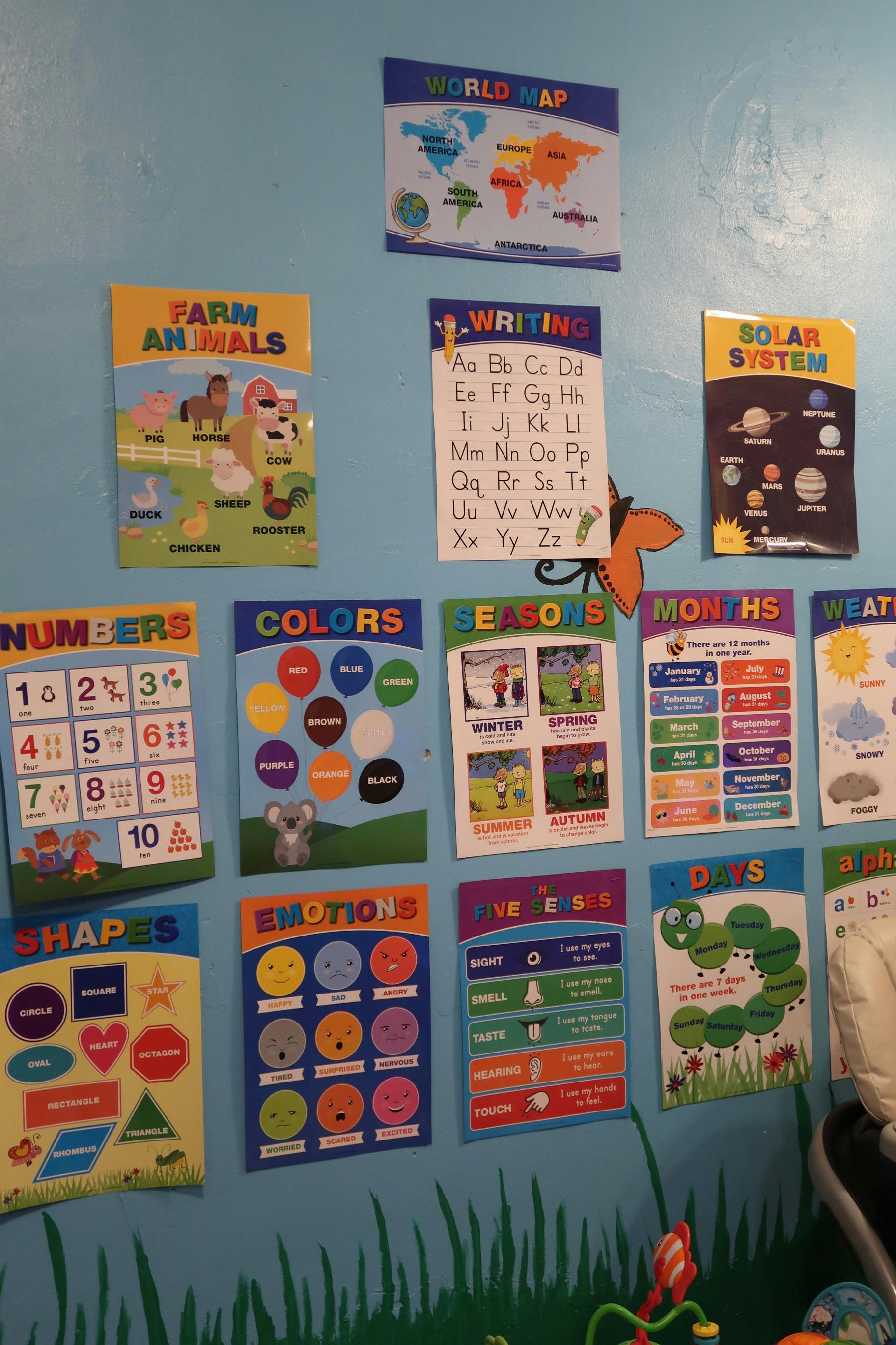 Educational posters on a wall, including world map, farm animals, numbers, and shapes