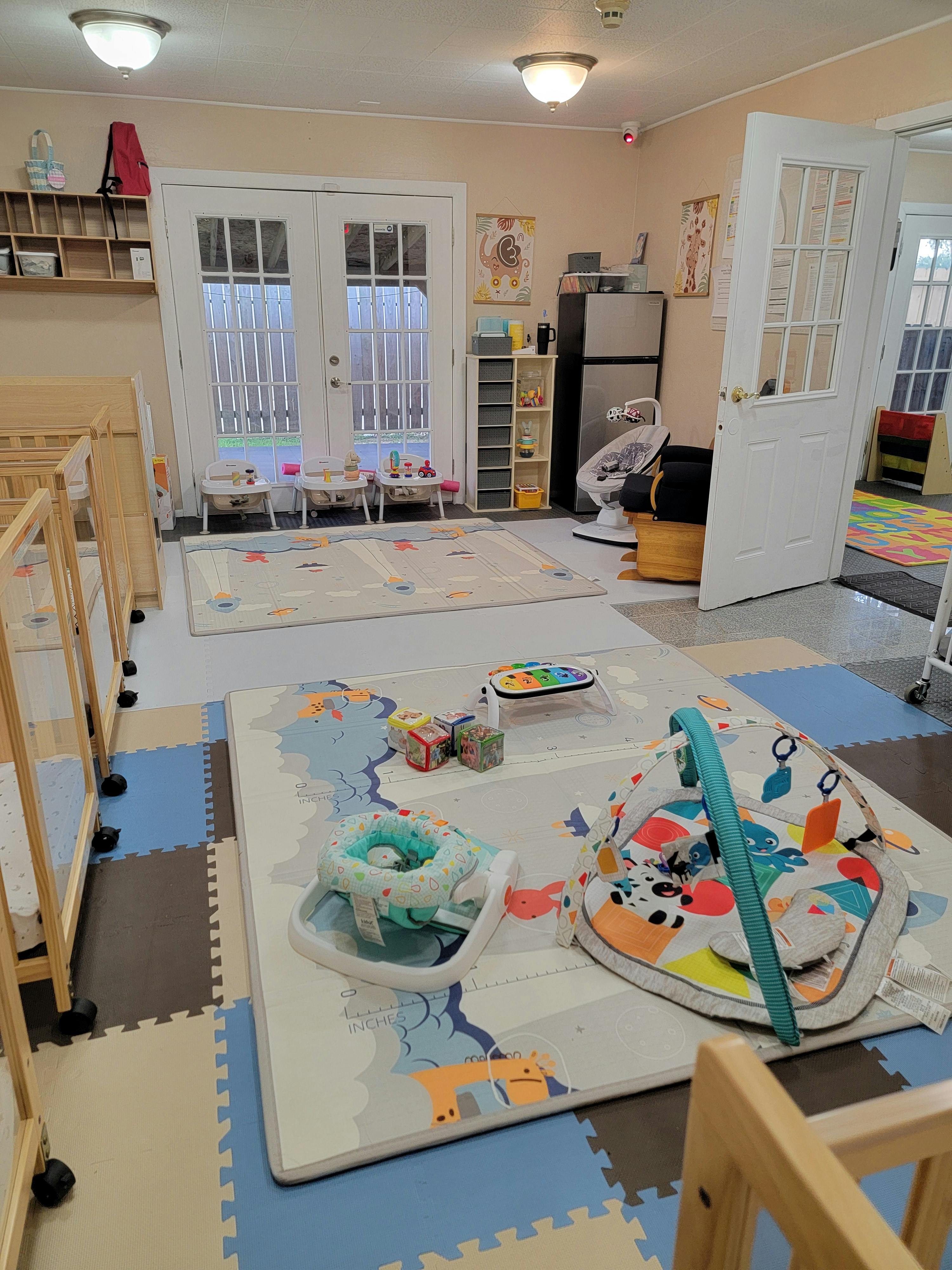 A playroom with multiple baby play mats, cribs, and toys, with light blue and grey walls