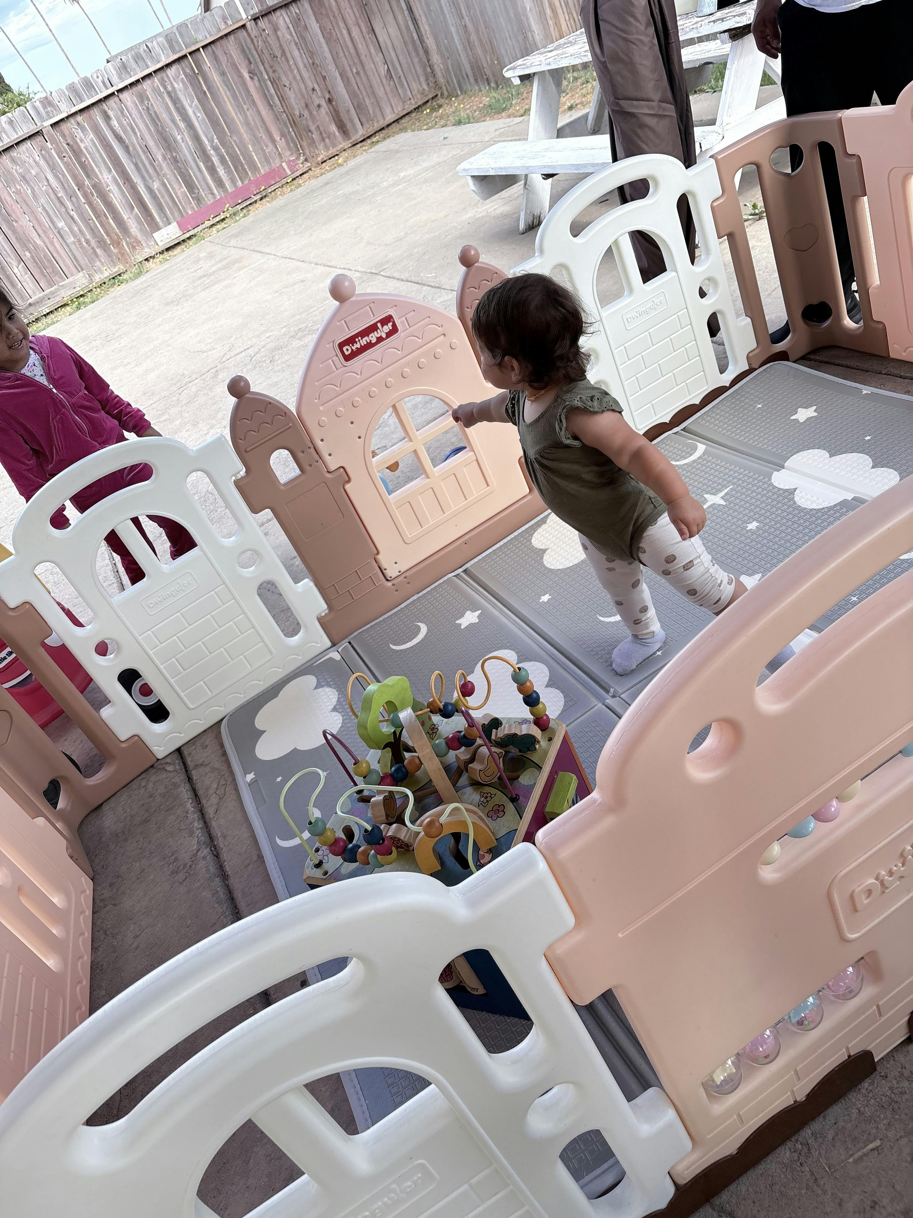 Child standing inside a playpen with a bead maze toy on a play mat