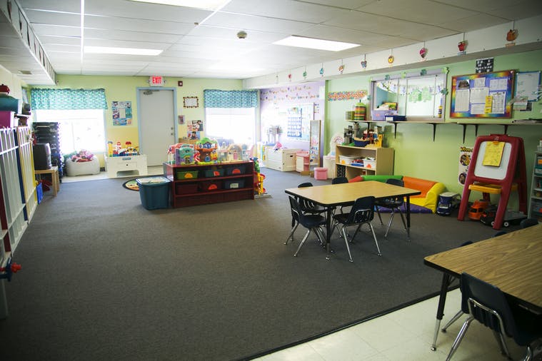 Empty classroom with small tables and chairs, toys, and learning materials
