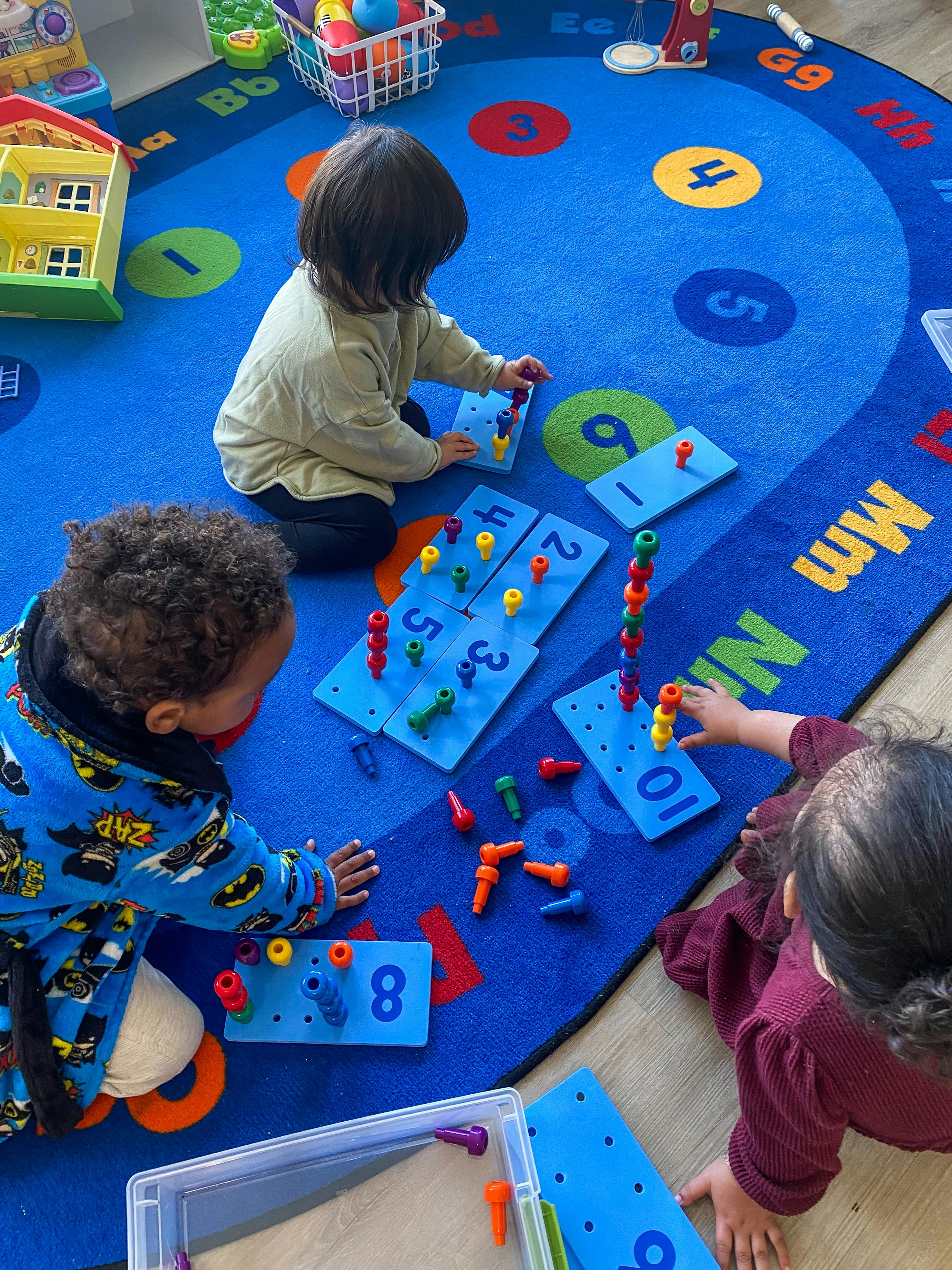 Three children playing with pegboards and pegs on a blue alphabet rug