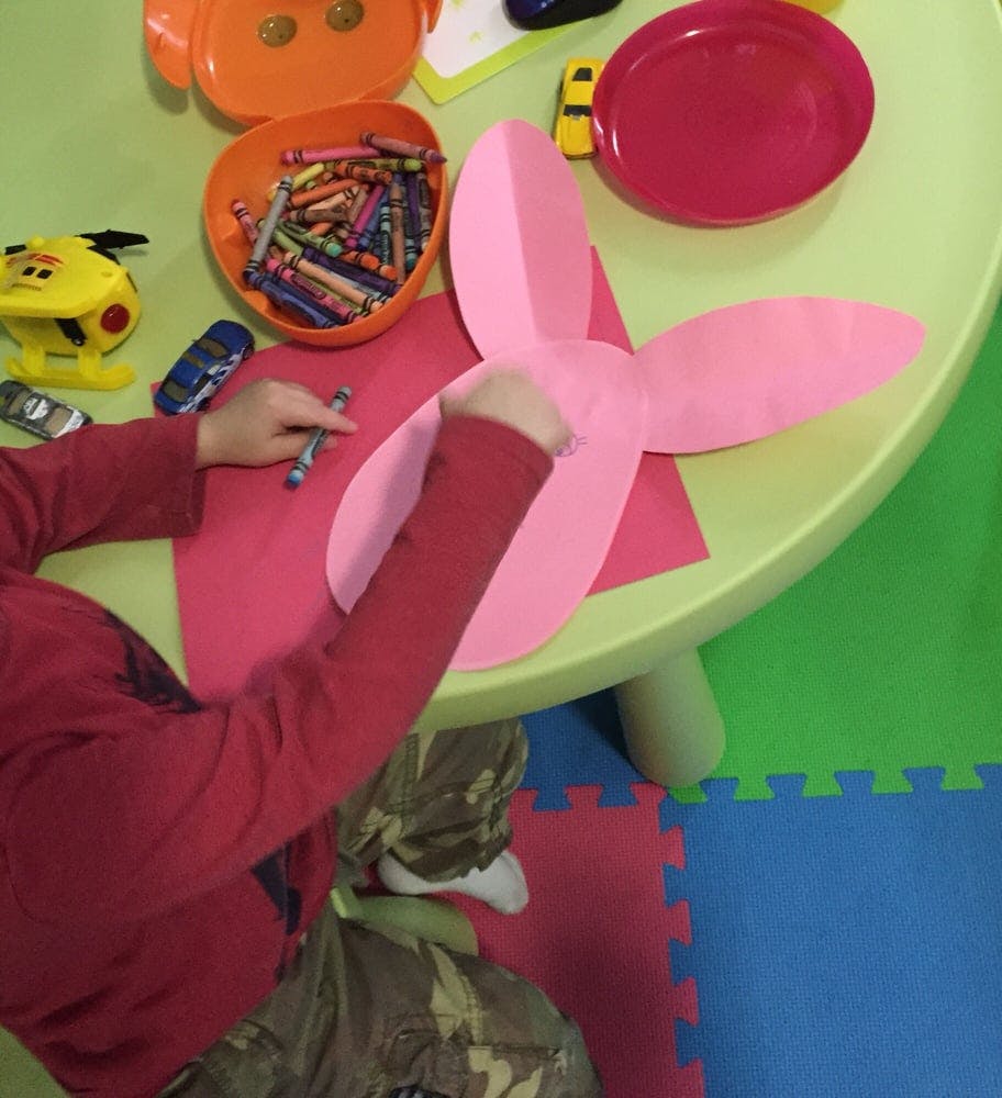 Child drawing on pink paper at a table with crayons