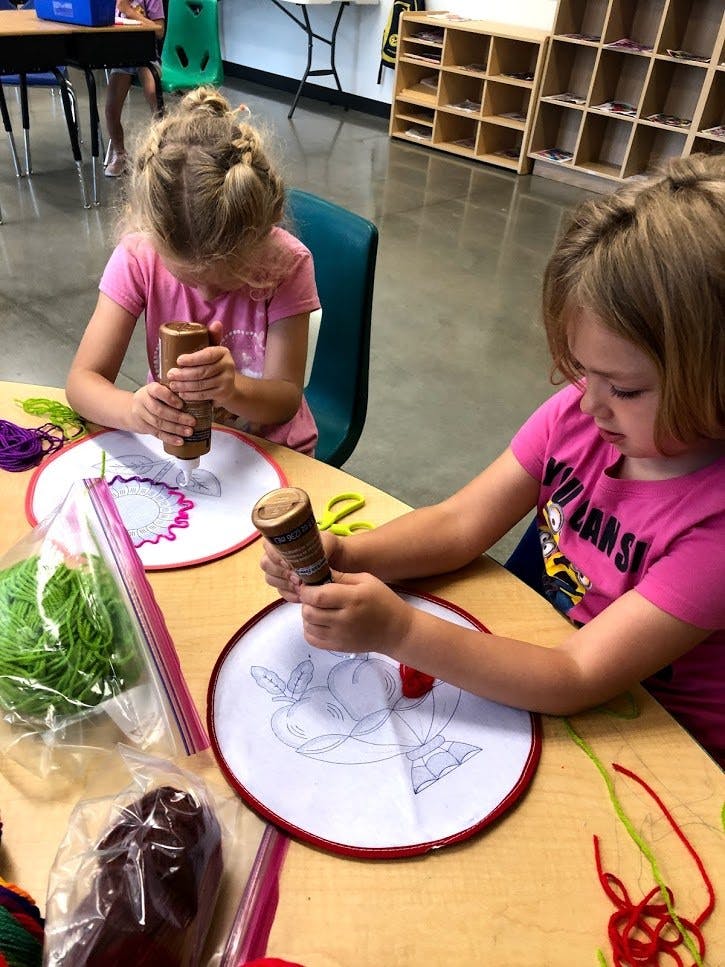 Two children applying glue to paper in a classroom