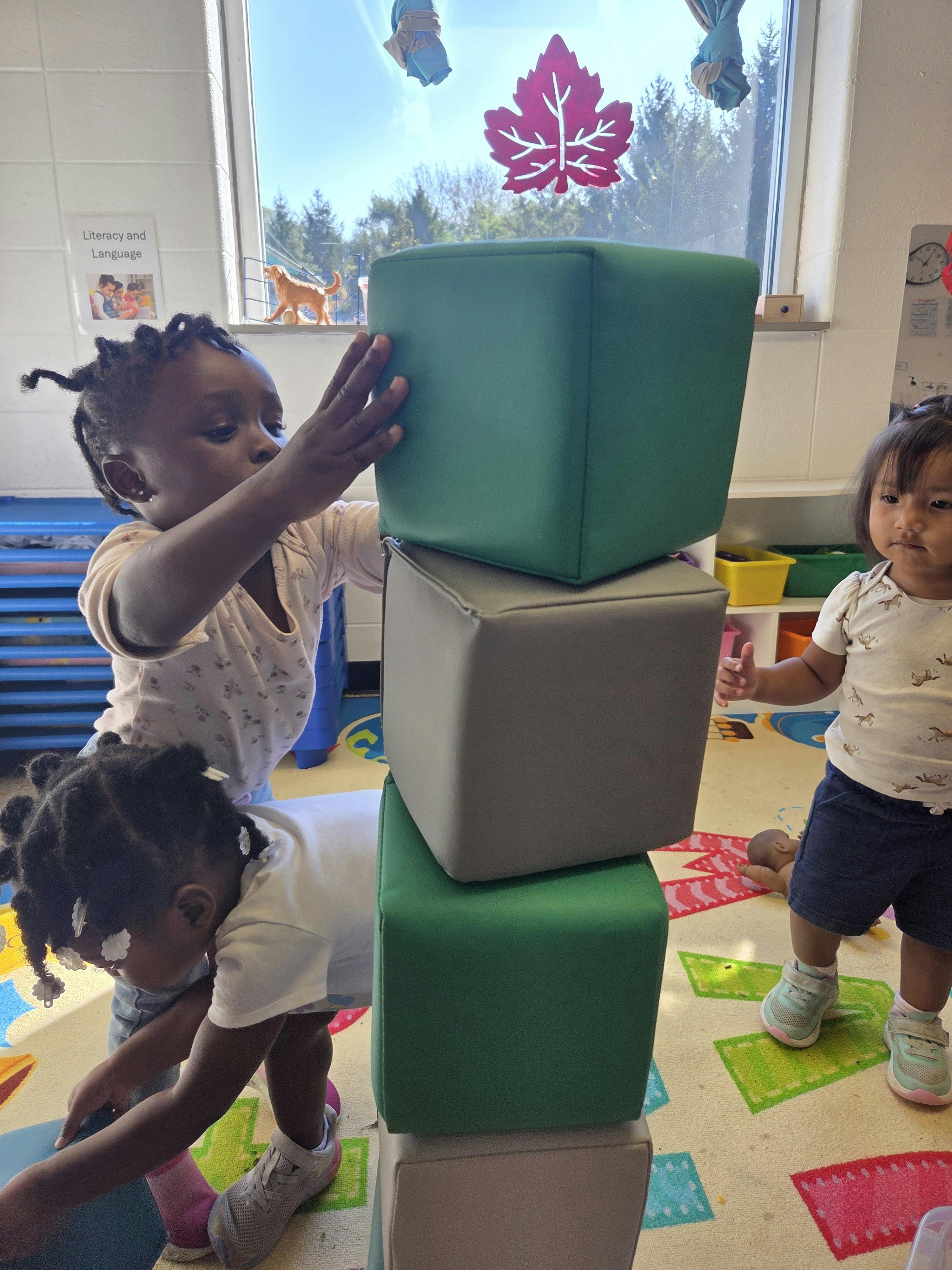 Three children playing with large soft blocks in a classroom