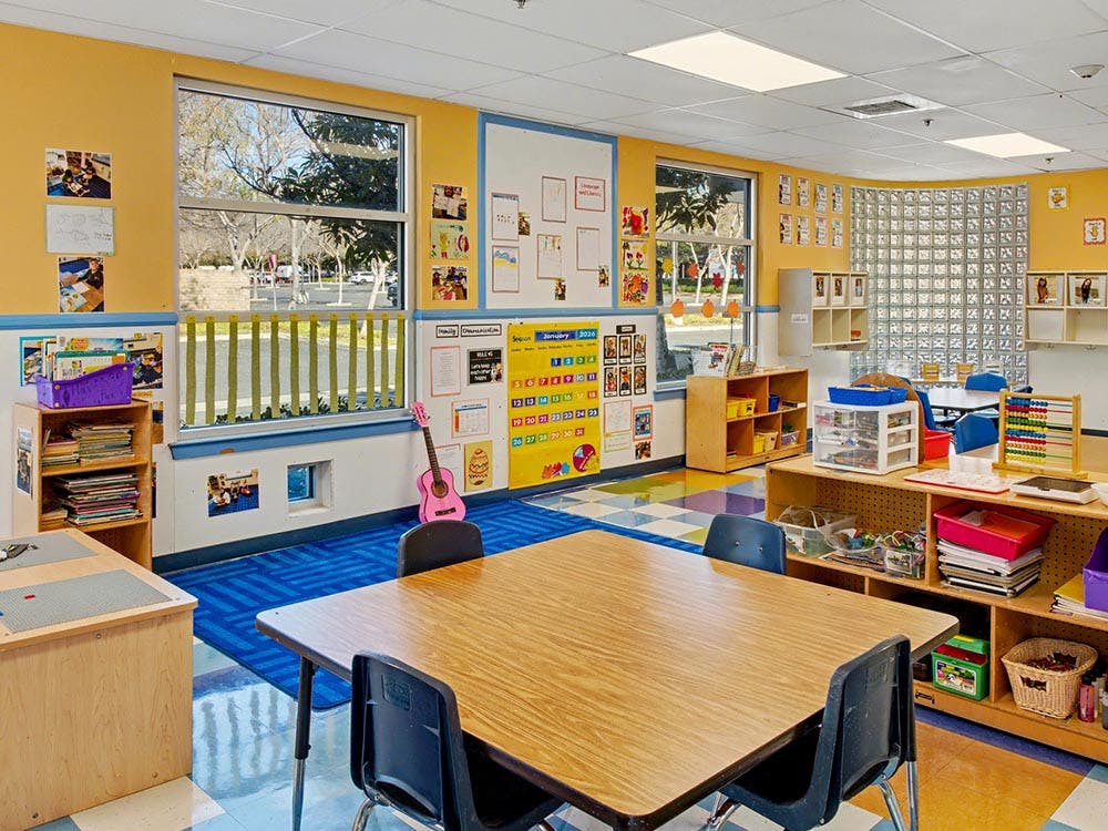 Classroom with tables, chairs, shelves, a calendar, and a pink toy guitar