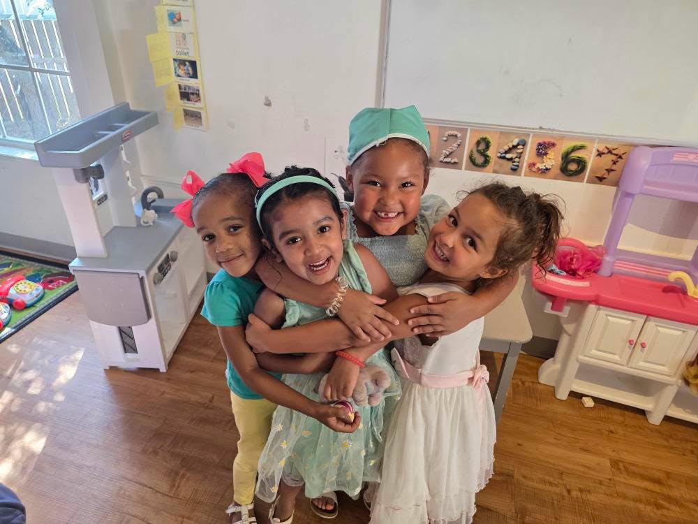 Group of four children hugging in a classroom