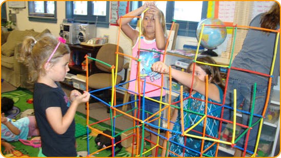 Children building a structure with colorful sticks and connectors in a classroom