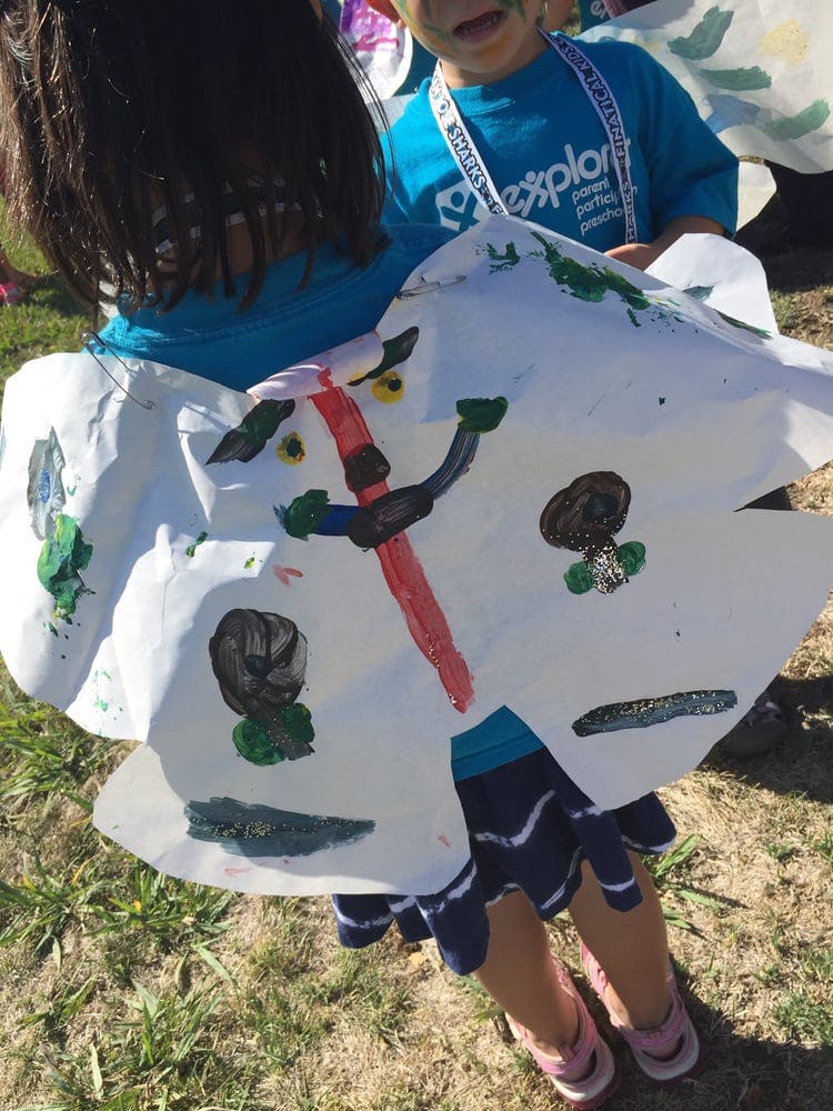Child holding a large paper cutout with painted designs