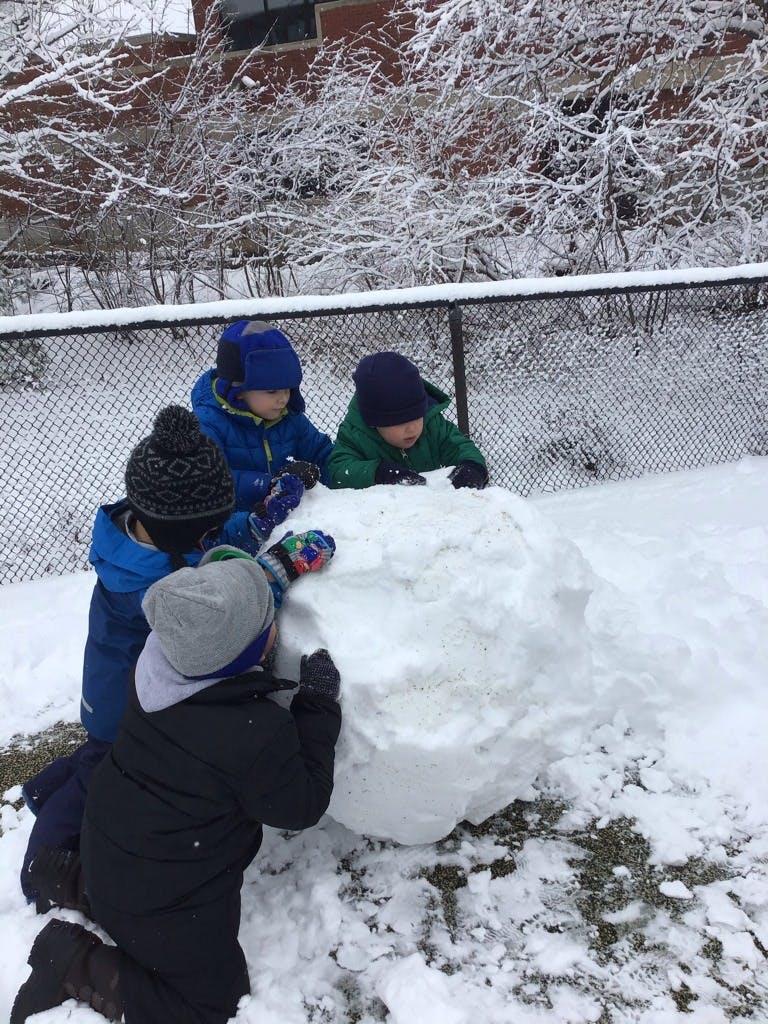 Four children building a large snowman in a snowy outdoor area