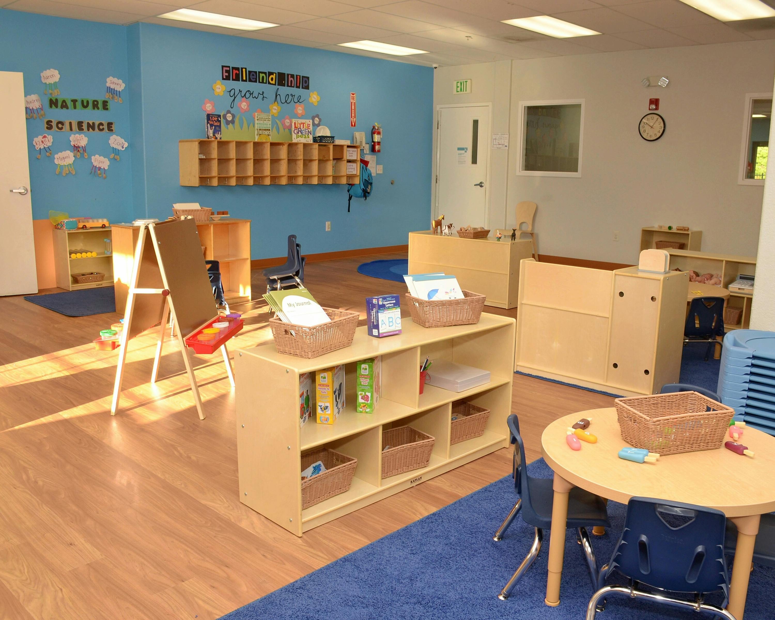 Classroom with small tables, chairs, and shelves with learning materials